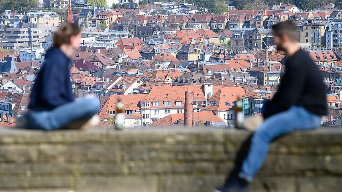 05.04.2020, Baden-Württemberg, Stuttgart: Eine junge Frau und ein junger Mann sitzen im Abstand von etwa eineinhalb Metern voneinander entfernt auf einer Mauer auf der Karlshöhe. Im Hintergrund sind die Dächer der Innenstadt zu sehen. Derzeit herrschen bestimmte Kontaktbeschränkungen, welche eine schnelle Ausbreitung des Virus bremsen sollen. Foto: Sebastian Gollnow/dpa +++ dpa-Bildfunk +++