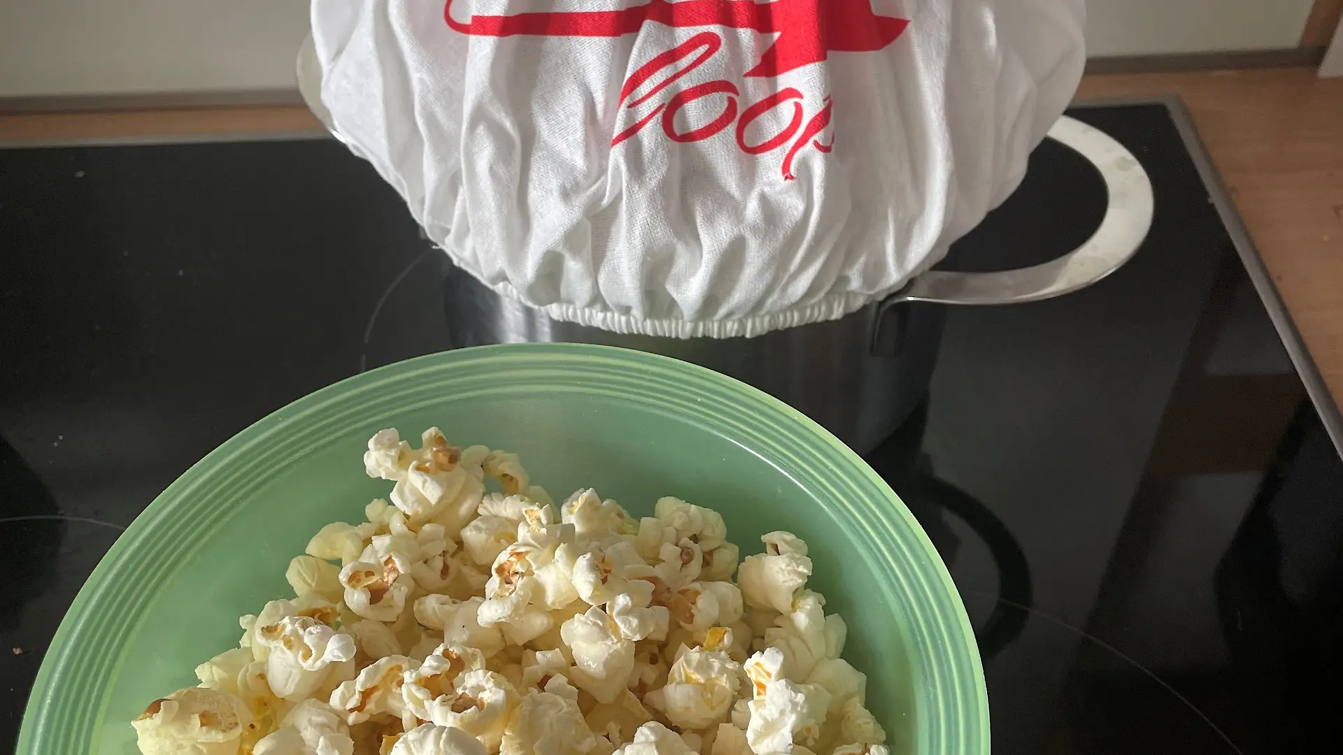 Über einen Kochtopf ist die Popcornloop Haube aufgezogen. Davor steht eine kleine Schüssel mit Popcorn.