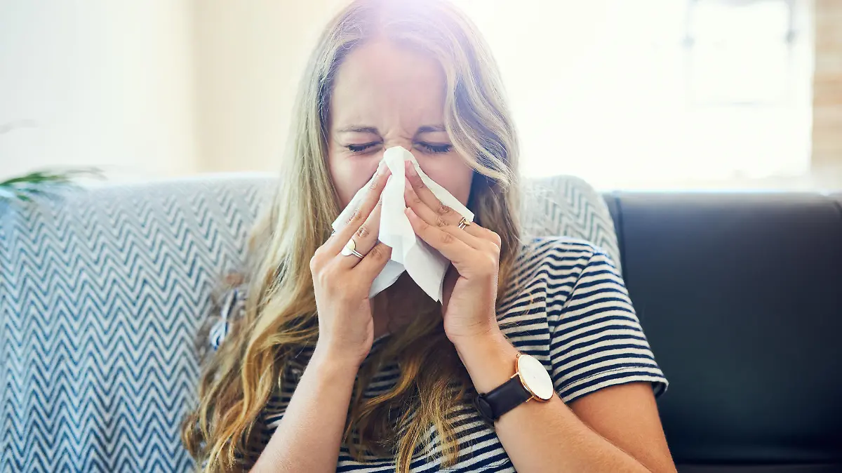 Shot of a young woman blowing her nose with a tissue at home