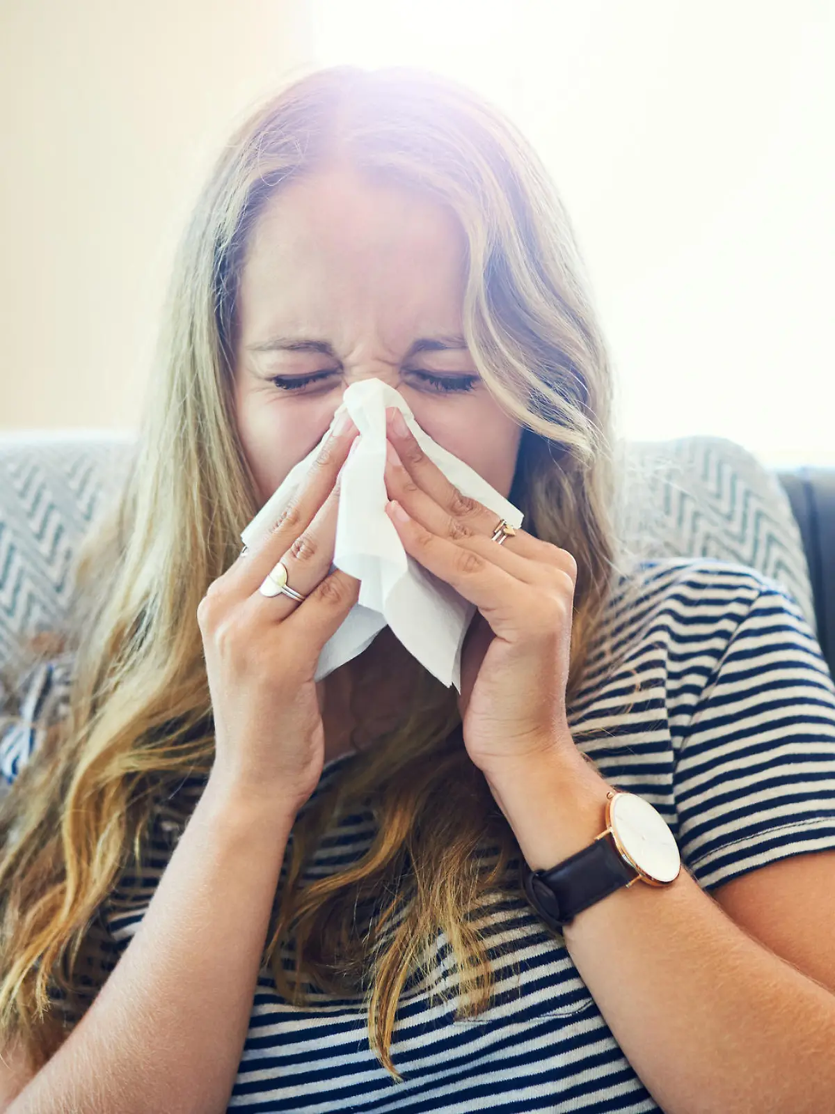Shot of a young woman blowing her nose with a tissue at home