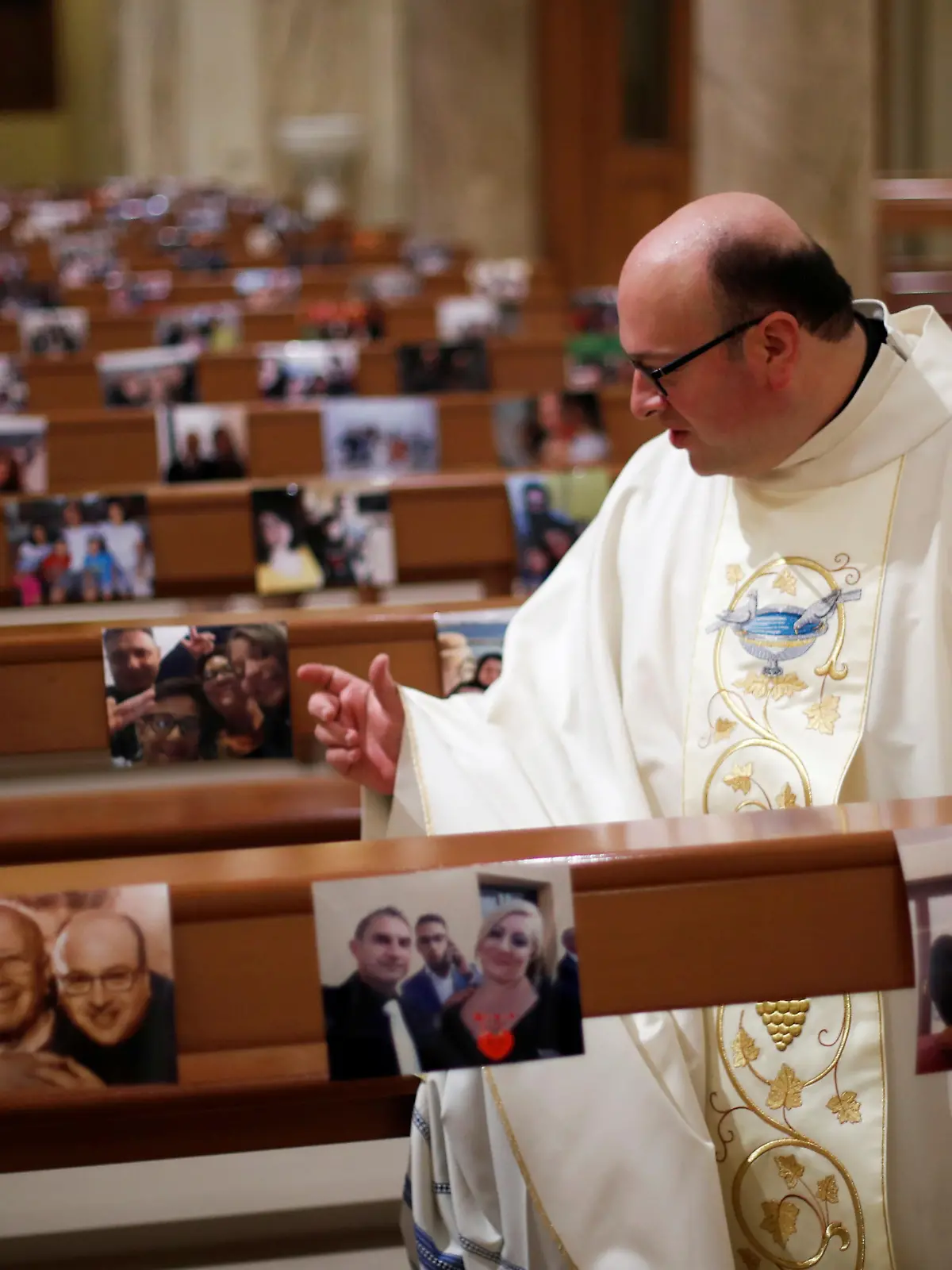 Priest Don Giancarlo Ruggieri gestures amid benches with pictures of members of the congregation, after livestreaming an Easter Sunday Mass, as Italy celebrates Easter under lockdown, due to the outbreak of the coronavirus disease (COVID-19), in the small southern town of San Giorgio Ionico, Itay April 12, 2020. REUTERS/Alessandro Garofalo