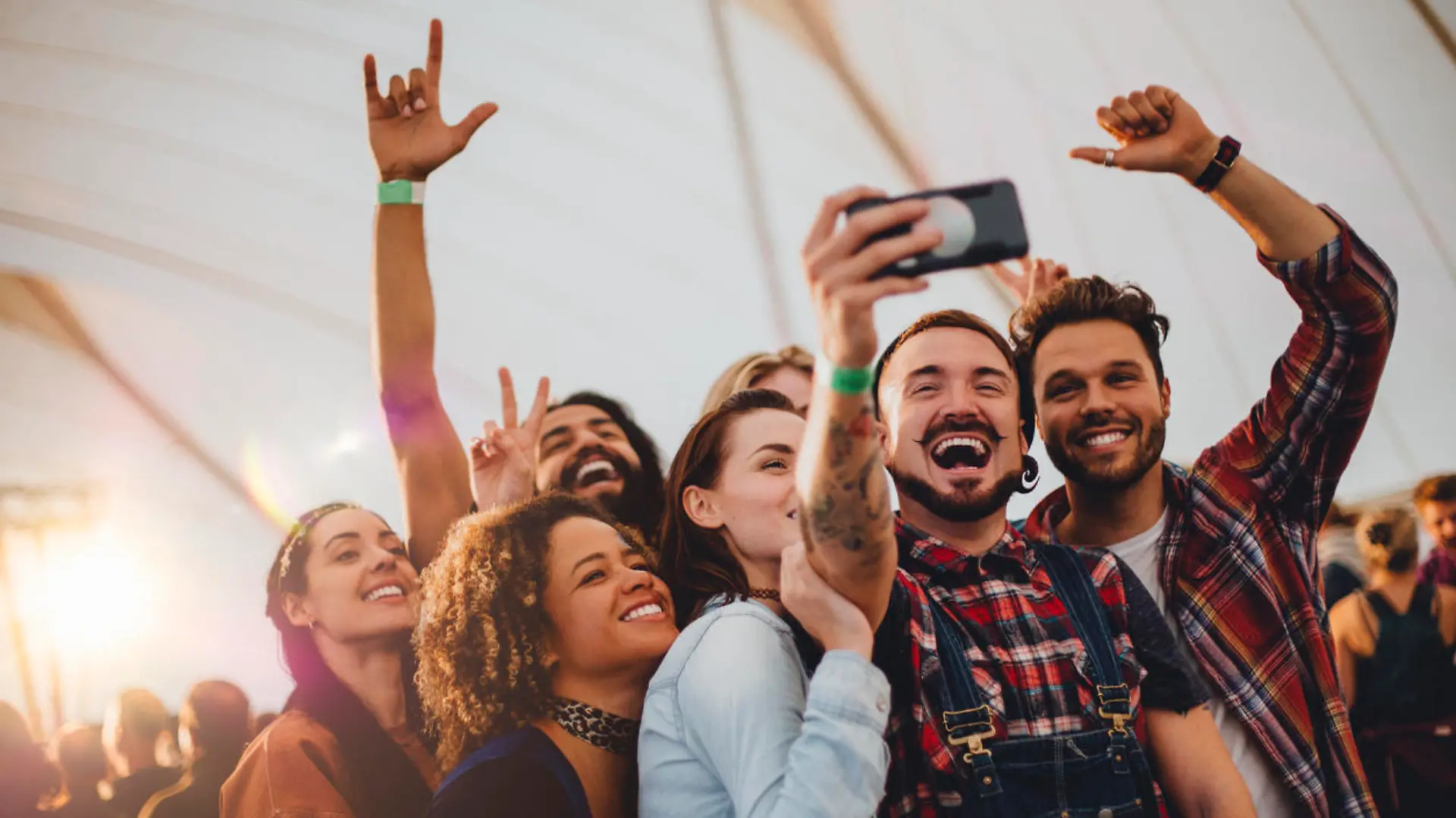 Group of young adult friends are taking a group selfie on a smartphone while they are at a festival.