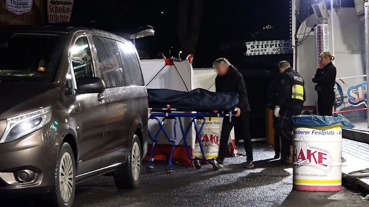 19.03.2023, Nordrhein-Westfalen, Münster: Ein Bestatter bringt den Toten mit einer Bahre in sein Fahrzeug. Ein 31 Jahre alter Mann ist nach einer Auseinandersetzung auf dem Send in Münster mit einem Messer niedergestochen worden und gestorben. Ein bislang unbekannter Täter war am Samstagabend auf der Kirmes an einem Karussell mit dem 31-Jährigen in Streit geraten. Foto: David Poggemann/Nord-West-Media /dpa +++ dpa-Bildfunk +++