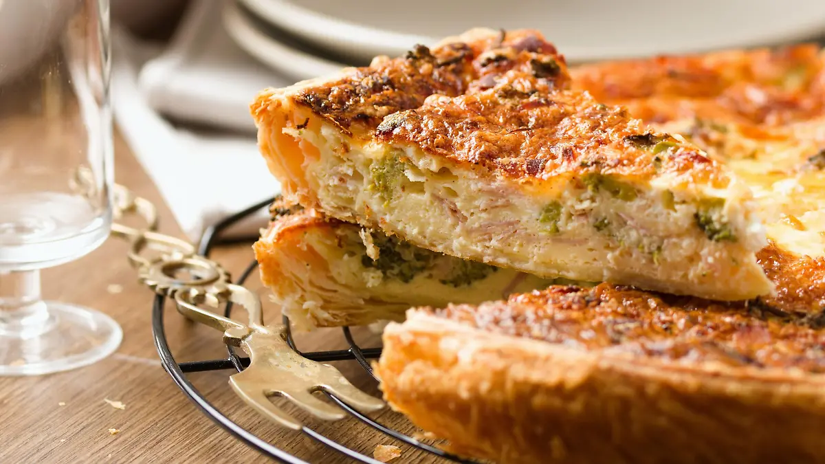 Quiche, french vegetable pie. Slice of quiche cut out from the whole pie. Set against background of plate stack and wine glass
