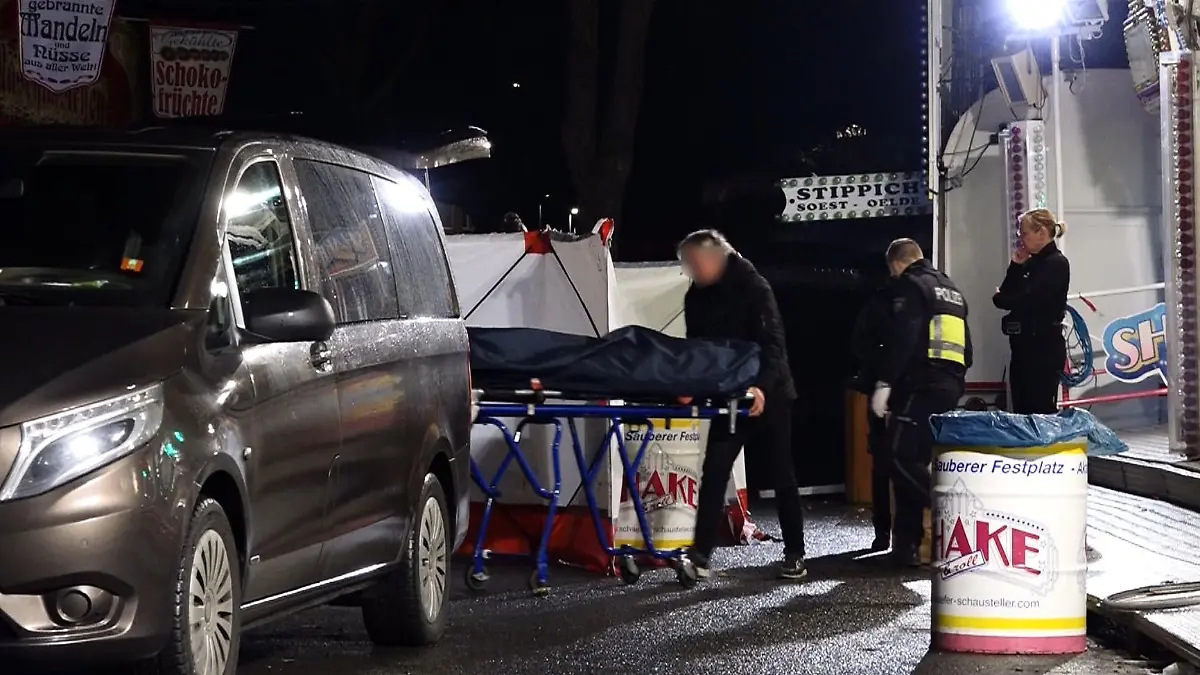 19.03.2023, Nordrhein-Westfalen, Münster: Ein Bestatter bringt den Toten mit einer Bahre in sein Fahrzeug. Ein 31 Jahre alter Mann ist nach einer Auseinandersetzung auf dem Send in Münster mit einem Messer niedergestochen worden und gestorben. Ein bislang unbekannter Täter war am Samstagabend auf der Kirmes an einem Karussell mit dem 31-Jährigen in Streit geraten. Foto: David Poggemann/Nord-West-Media /dpa +++ dpa-Bildfunk +++