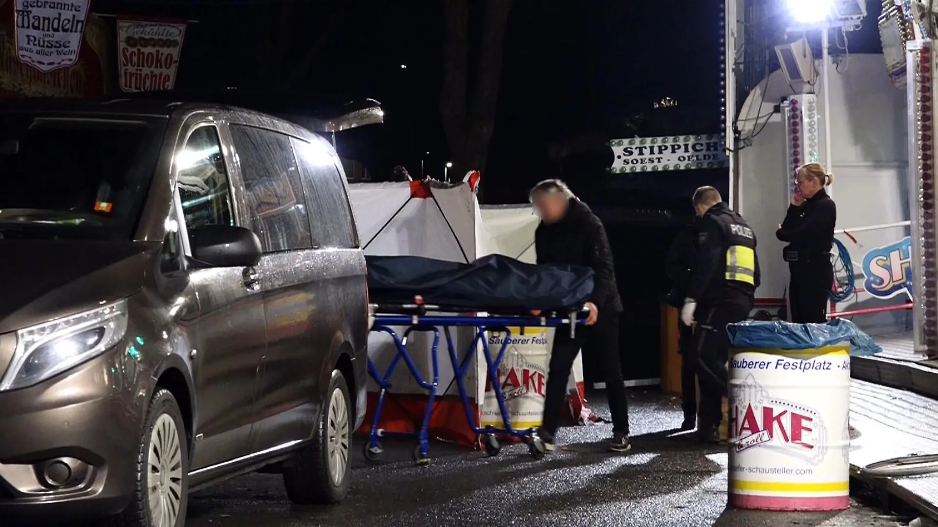 19.03.2023, Nordrhein-Westfalen, Münster: Ein Bestatter bringt den Toten mit einer Bahre in sein Fahrzeug. Ein 31 Jahre alter Mann ist nach einer Auseinandersetzung auf dem Send in Münster mit einem Messer niedergestochen worden und gestorben. Ein bislang unbekannter Täter war am Samstagabend auf der Kirmes an einem Karussell mit dem 31-Jährigen in Streit geraten. Foto: David Poggemann/Nord-West-Media /dpa +++ dpa-Bildfunk +++