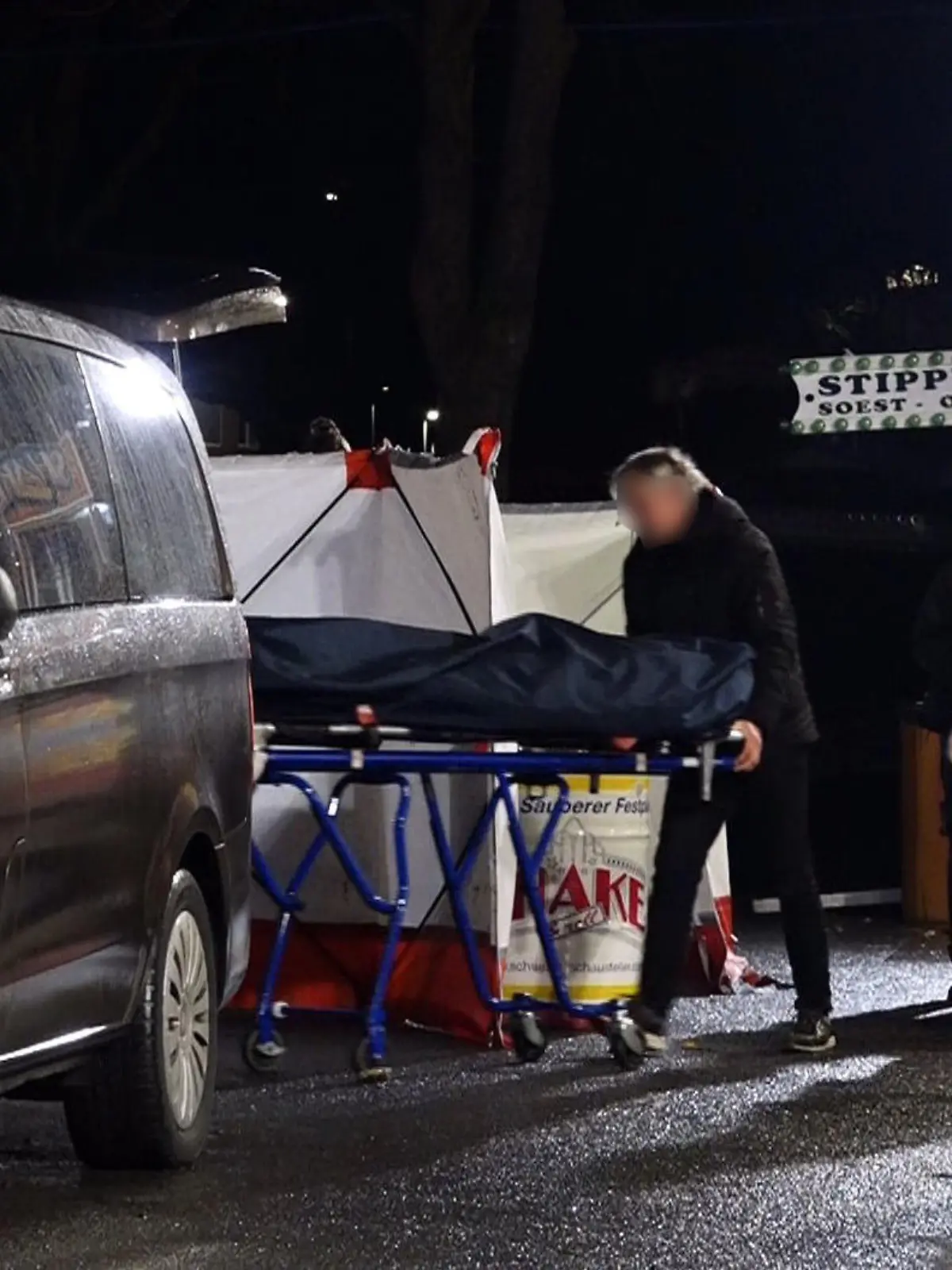 19.03.2023, Nordrhein-Westfalen, Münster: Ein Bestatter bringt den Toten mit einer Bahre in sein Fahrzeug. Ein 31 Jahre alter Mann ist nach einer Auseinandersetzung auf dem Send in Münster mit einem Messer niedergestochen worden und gestorben. Ein bislang unbekannter Täter war am Samstagabend auf der Kirmes an einem Karussell mit dem 31-Jährigen in Streit geraten. Foto: David Poggemann/Nord-West-Media /dpa +++ dpa-Bildfunk +++