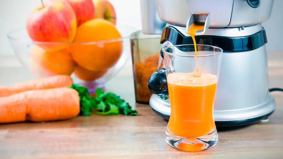 Juicer and carrot juice. Fruits in background