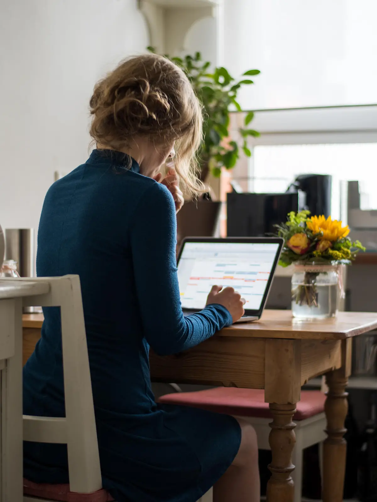 Blonde junge Frau sitzt am Tisch in der heimischen Küche, während der Arbeit an einem laptop