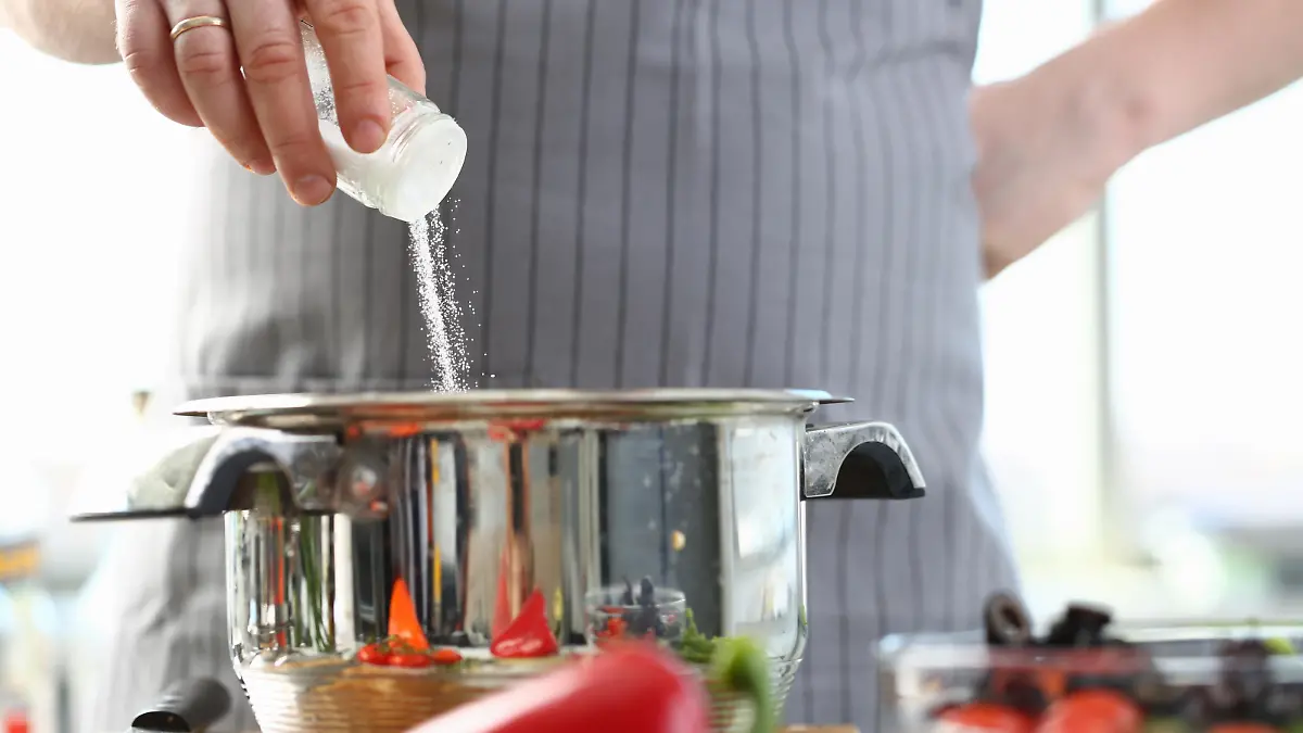 Culinary Chef Adding Saucepan White Sea Salt. Man in Apron Holding Spice Shaker in Hand. Male Fingers Putting Ingredient to Stainless Pan. Cooking in Kitchen at Home Horizontal Photography