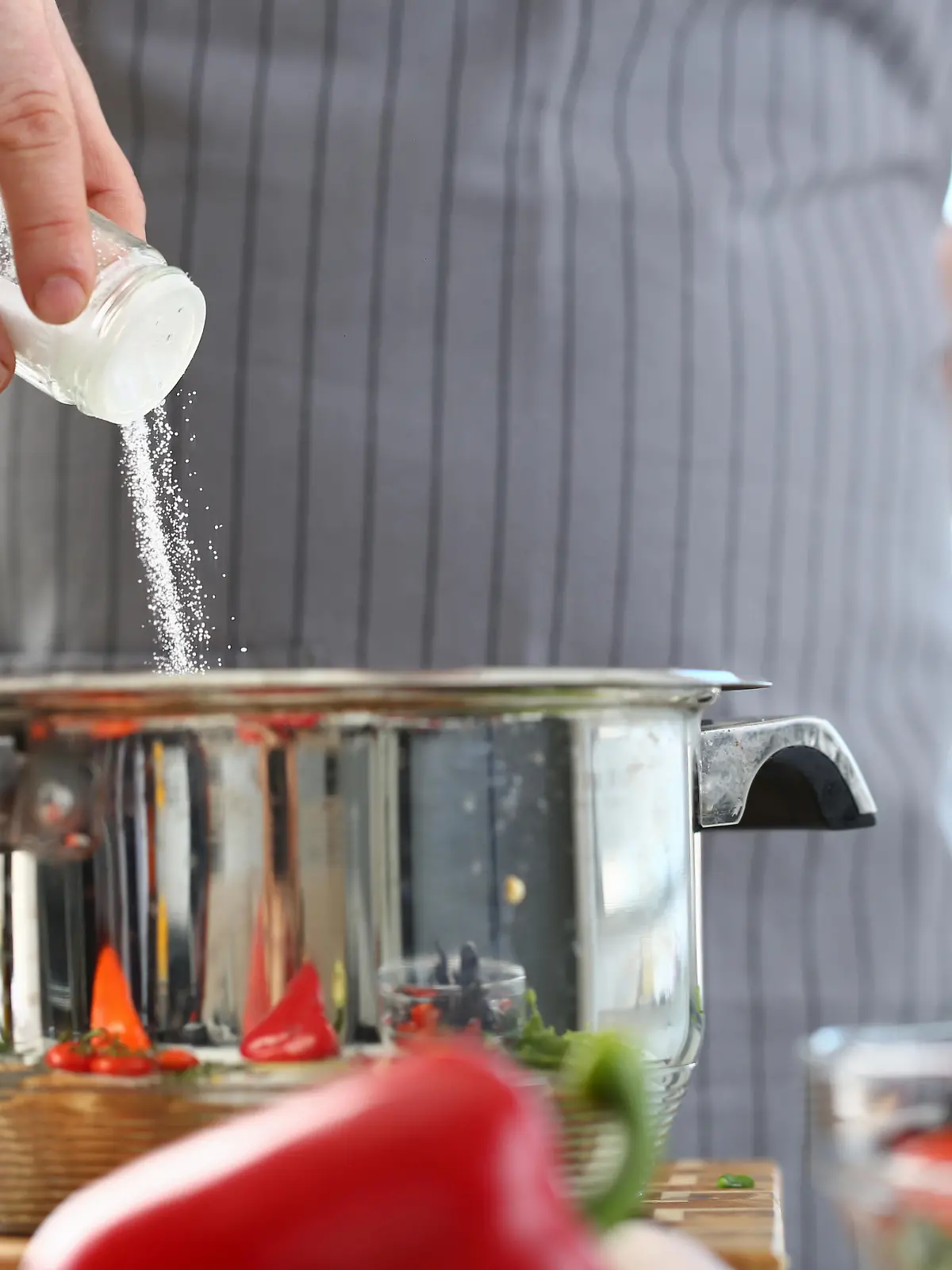 Culinary Chef Adding Saucepan White Sea Salt. Man in Apron Holding Spice Shaker in Hand. Male Fingers Putting Ingredient to Stainless Pan. Cooking in Kitchen at Home Horizontal Photography