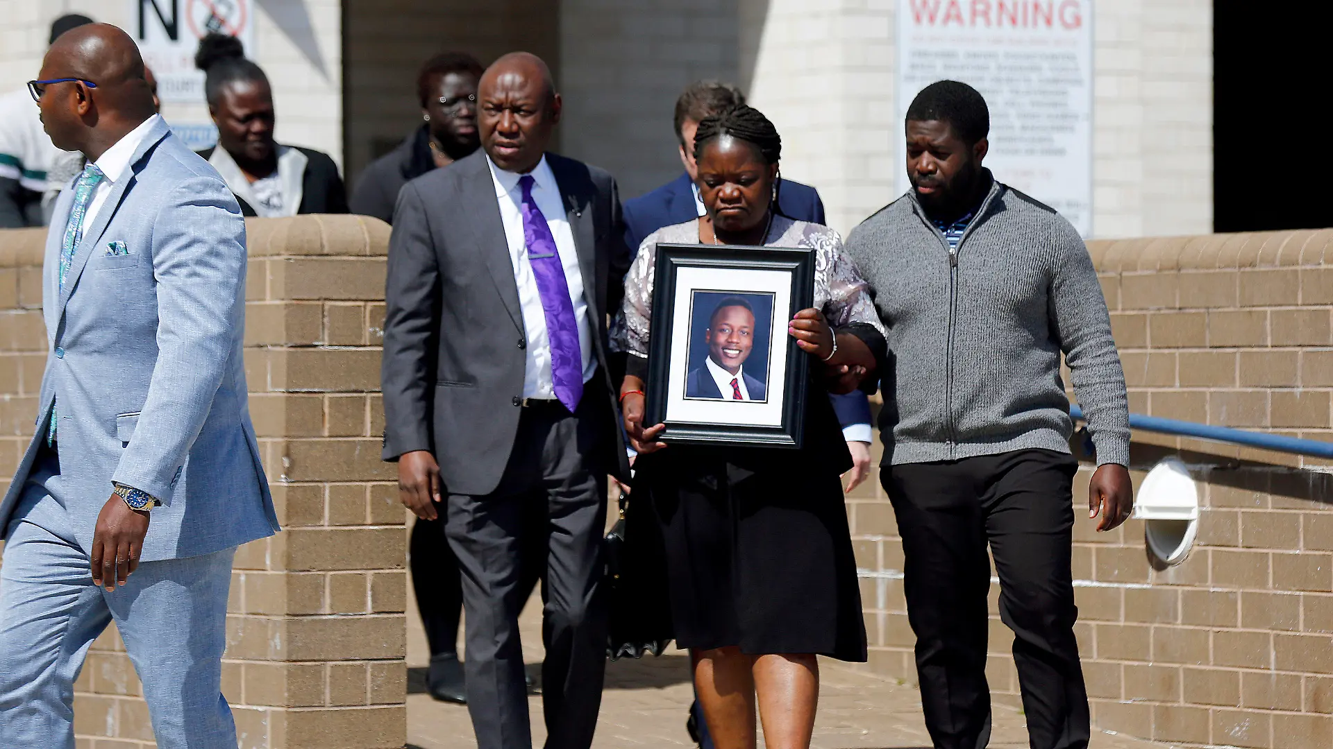 16.03.2023, USA, Dinwiddie: Caroline Ouko, Mutter von Irvo Otieno, hält ein Porträt ihres Sohnes, als sie zusammen mit ihrem Anwalt Ben Crump (M, l) und ihrem älteren Sohn Leon Ochieng das Dinwiddie Courthouse verlässt. Anderthalb Wochen nach dem brutalen Tod eines 28-jährigen Schwarzen in einer psychiatrischen Klinik im US-Bundesstaat Virginia haben seine Angehörigen schwere Vorwürfe gegen die Polizei erhoben. Foto: Daniel Sangjib Min/Richmond Times-Dispatch/AP +++ dpa-Bildfunk +++