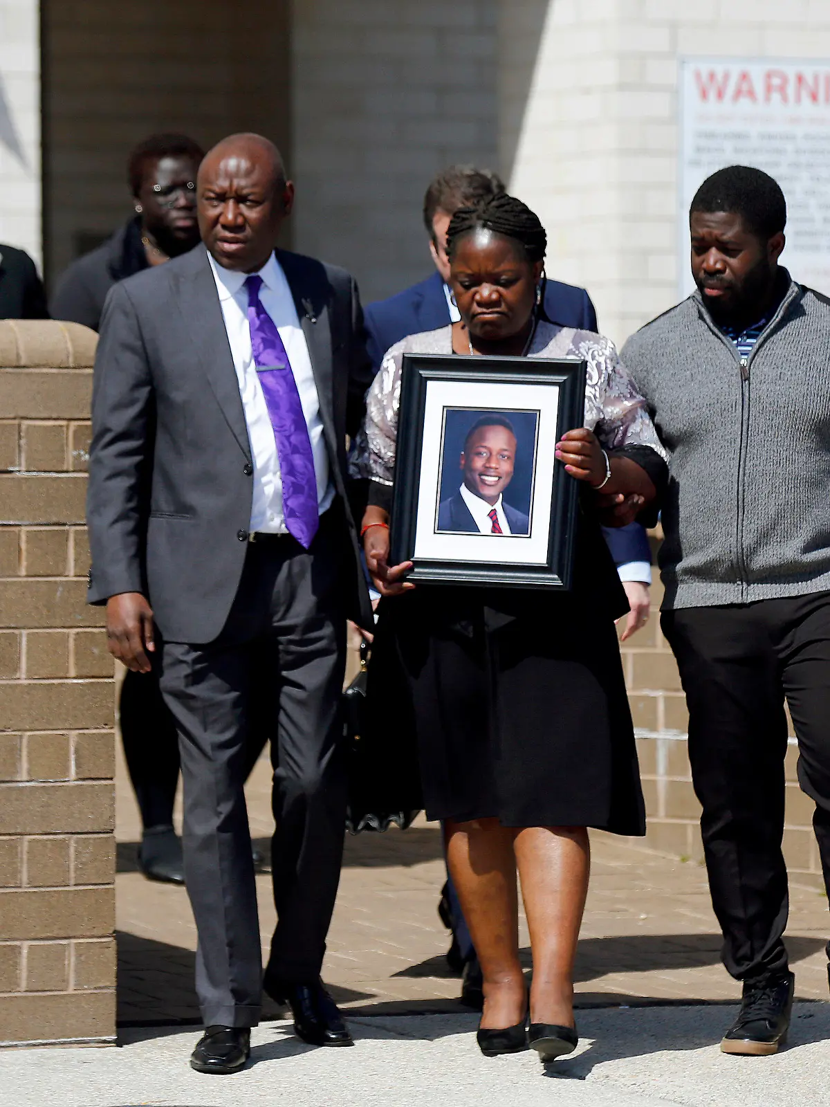 16.03.2023, USA, Dinwiddie: Caroline Ouko, Mutter von Irvo Otieno, hält ein Porträt ihres Sohnes, als sie zusammen mit ihrem Anwalt Ben Crump (M, l) und ihrem älteren Sohn Leon Ochieng das Dinwiddie Courthouse verlässt. Anderthalb Wochen nach dem brutalen Tod eines 28-jährigen Schwarzen in einer psychiatrischen Klinik im US-Bundesstaat Virginia haben seine Angehörigen schwere Vorwürfe gegen die Polizei erhoben. Foto: Daniel Sangjib Min/Richmond Times-Dispatch/AP +++ dpa-Bildfunk +++