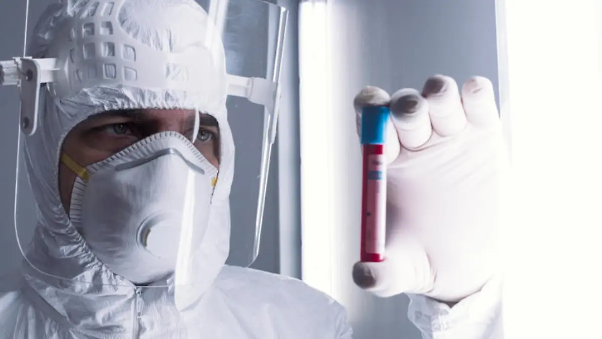 Ein Labormitarbeiter im Schutzanzug hält ein kleines Röhrchen mit Blut gefüllt gegen das Licht, um es sich anzuschauen