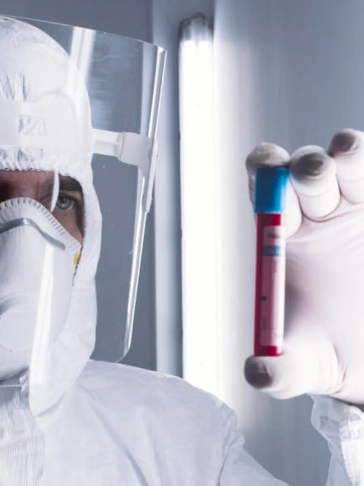 Ein Labormitarbeiter im Schutzanzug hält ein kleines Röhrchen mit Blut gefüllt gegen das Licht, um es sich anzuschauen
