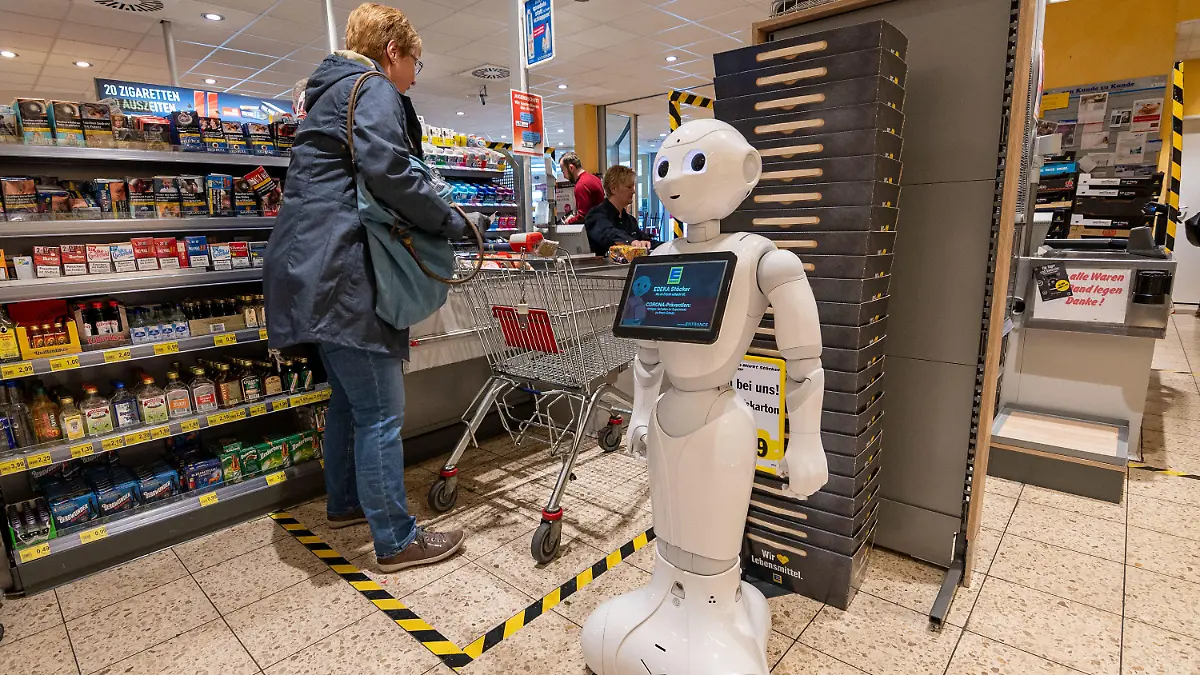 28.03.2020, Nordrhein-Westfalen, Lindlar: Pflegeroboter «Pepper» steht im Kassenbereich des Edeka-Marktes und weist Kunden darauf hin, Abstand zu halten und sich vor einer Ansteckung mit dem Coronavirus zu schützen. Außerdem wirbt er für Rücksichtnahme und Solidarität untereinander und rät mit kindlich-freundlichem «Gesichtsausdruck» von Hamsterkäufen ab. (zu dpa "Abstand wahren: Roboter spricht Kunden in Kassenzone an") Foto: Markus Klümper/dpa +++ dpa-Bildfunk +++
