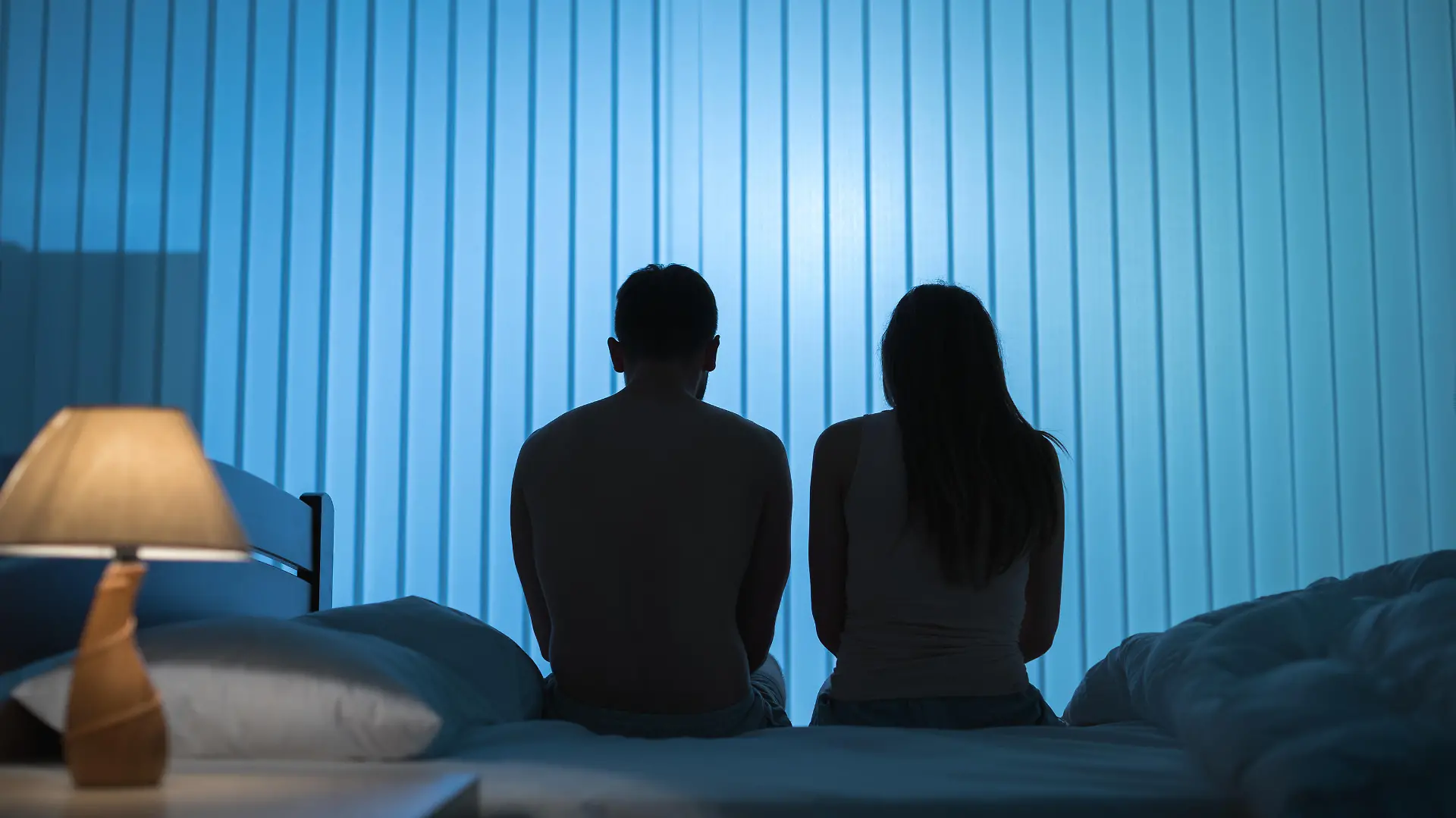 The man and woman sit on the bed. night time