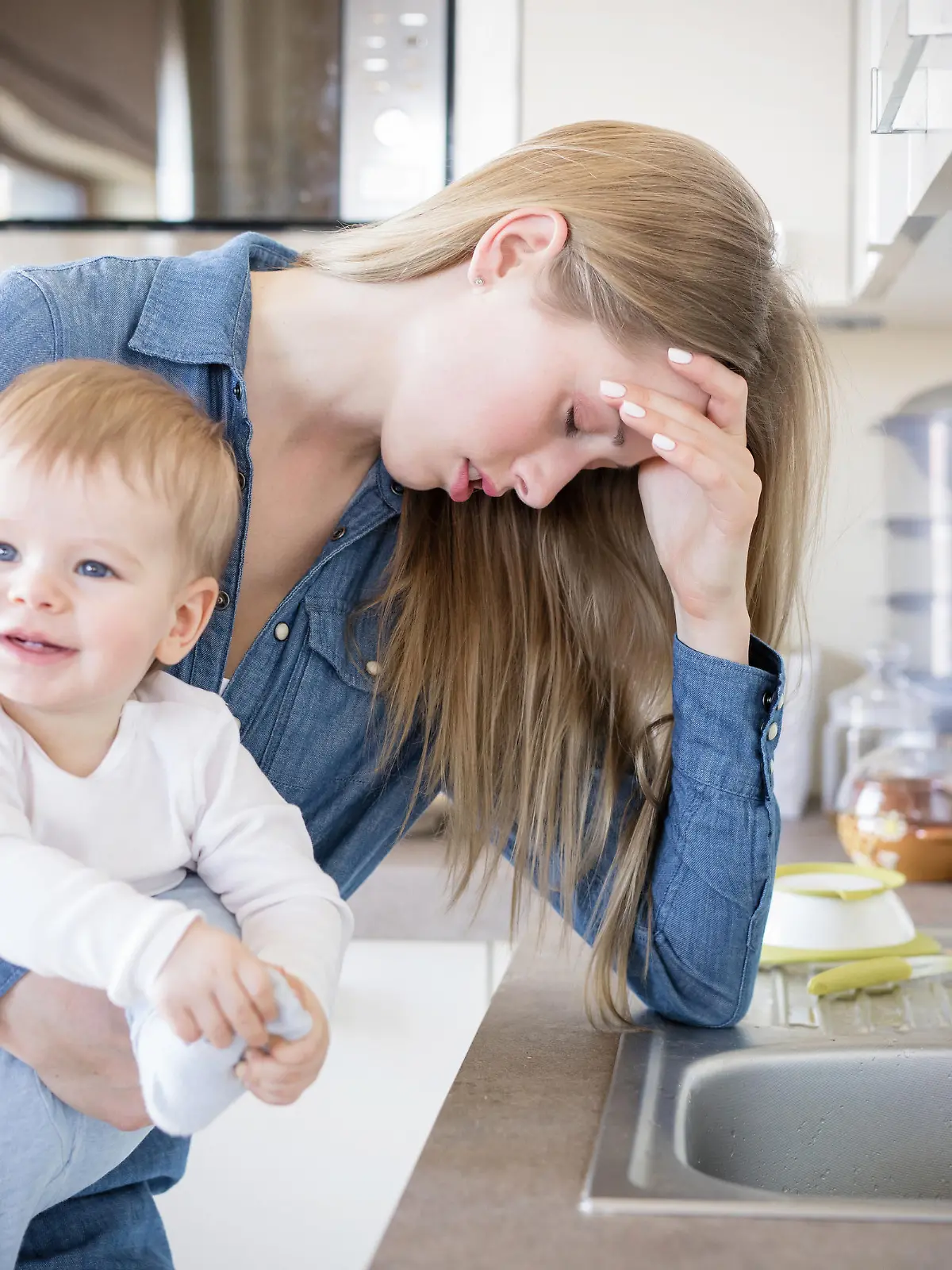 Mutter mit Kopfschmerzen hält ihr Baby.
