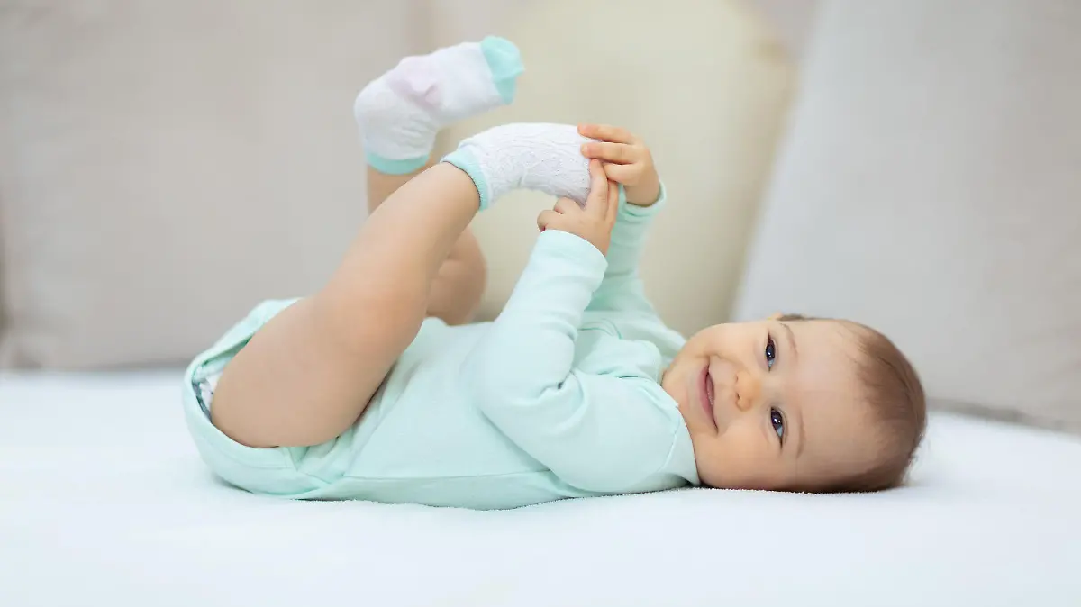Baby liegt im Babybody auf dem Bett und lächelt