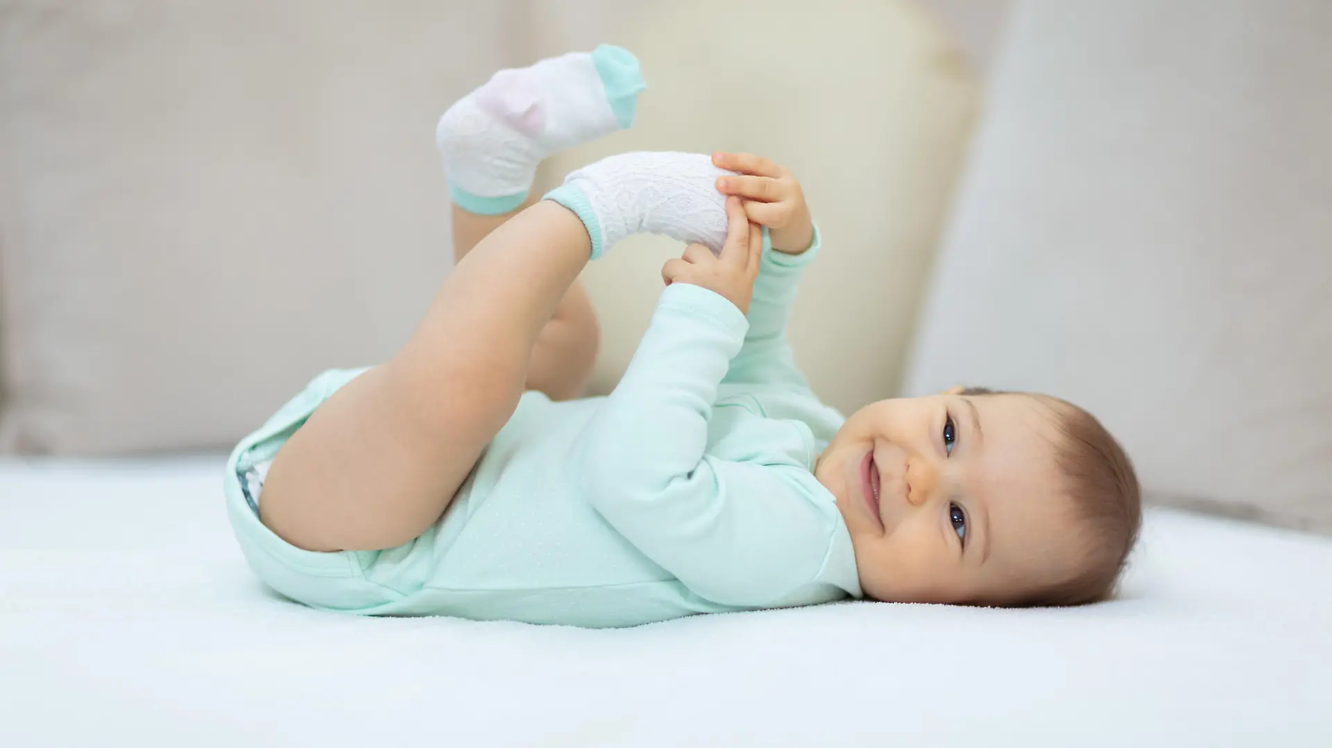 Baby liegt im Babybody auf dem Bett und lächelt