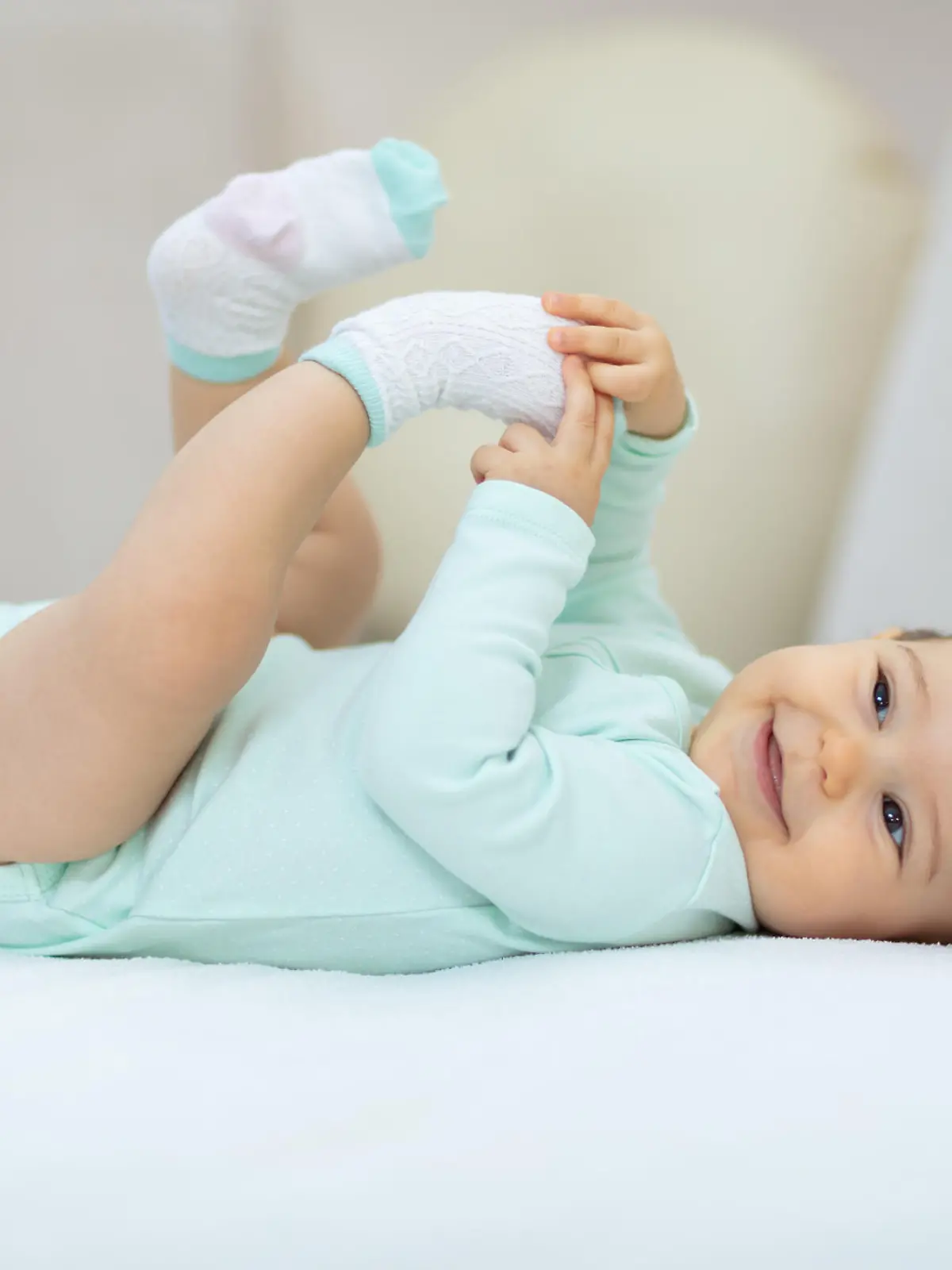 Baby liegt im Babybody auf dem Bett und lächelt