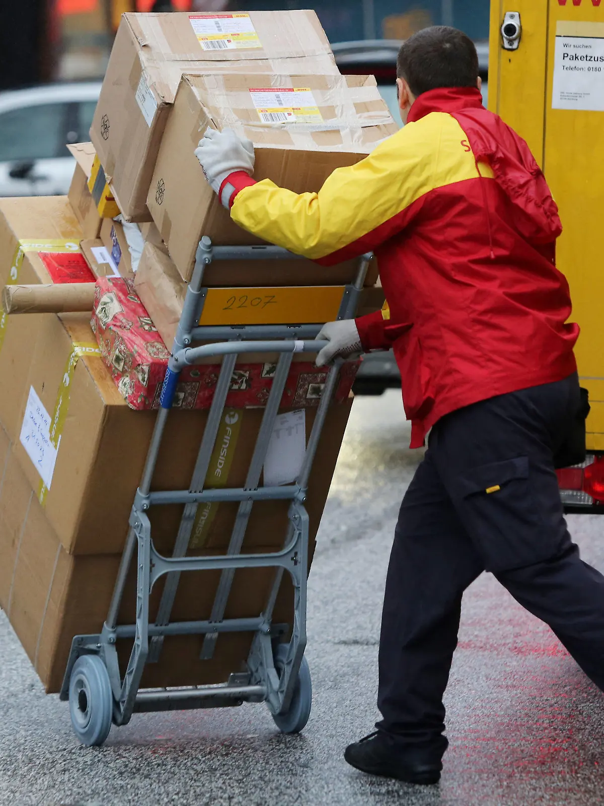 ARCHIV - 24.12.2014, Hamburg: Ein Paketbote von DHL liefert Päckchen aus. Wer in Deutschland ein Paket nach Hause bestellt, könnte dafür langfristig mehr bezahlen müssen. (zu dpa «Paketbranche erwägt Preisaufschlag für Haustür-Bestellungen») Foto: Malte Christians/dpa +++ dpa-Bildfunk +++