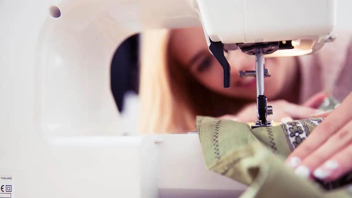 Closeup portrait of female designer using sewing machine in workshop. Focus on machine