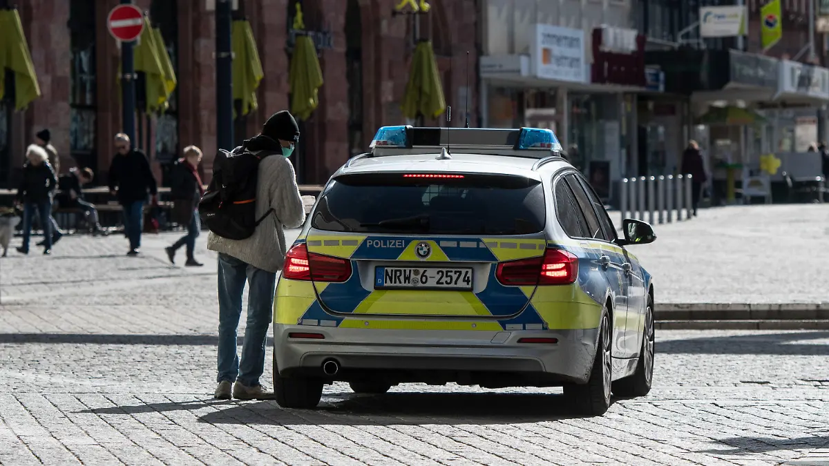 ARCHIV - 23.03.2020, Nordrhein-Westfalen, Dortmund: Ein Mann mit einem Mundschutz unterhält sich in der Fußgängerzone mit den Polizisten in einem Streifenwagen. Nordrhein-Westfalen hat einen Bußgeldkatalog für Verstöße gegen die landesweiten Corona-Regeln mit Strafen bis zu 5000 Euro erlassen. Im Wiederholungsfall werden sogar bis zu 25 000 Euro fällig. Der Erlass, der nach dpa-Informationen am Montagabend an die zuständigen Behörden geschickt wurde, liegt der Deutschen Presse-Agentur vor. Foto: Bernd Thissen/dpa +++ dpa-Bildfunk +++