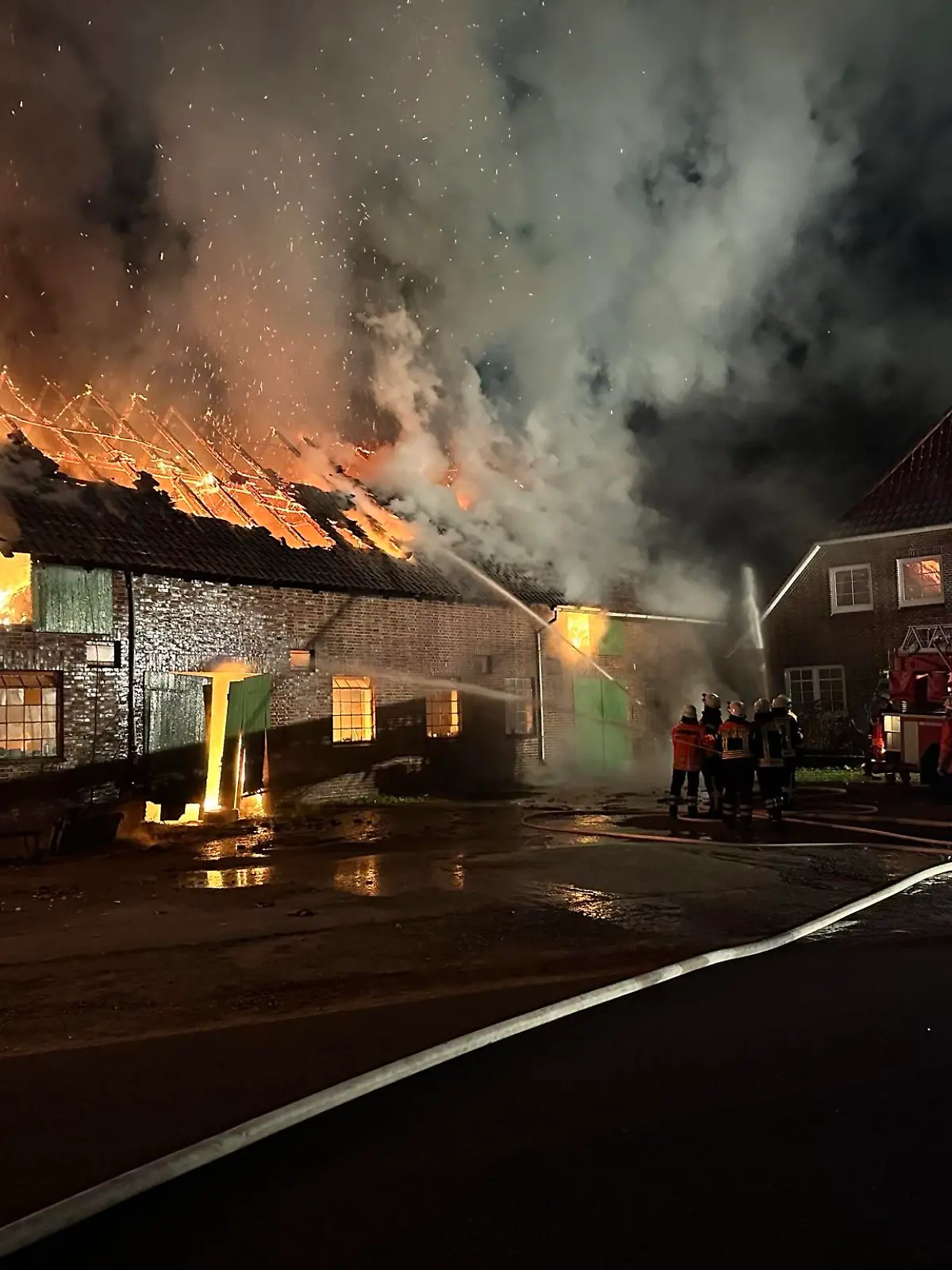 Blick auf die Scheune mit dem Wohnhaus im Hintergrund. Die Drehleiter aus Zeven wird gerade in Stellung gebracht