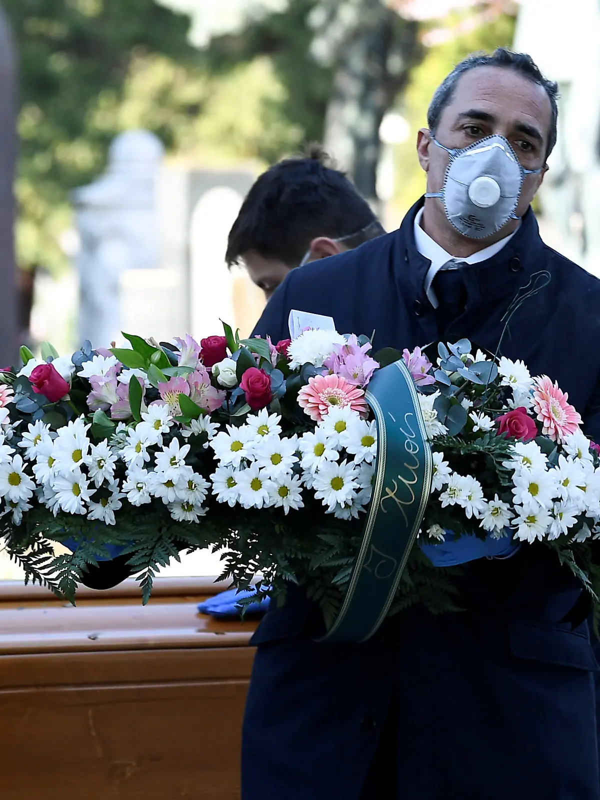 FILE PHOTO: Cemetery workers and funeral agency workers in protective masks transport a coffin of a person who died from coronavirus disease (COVID-19), into a cemetery in Bergamo, Italy March 16, 2020. REUTERS/Flavio Lo Scalzo/File Photo