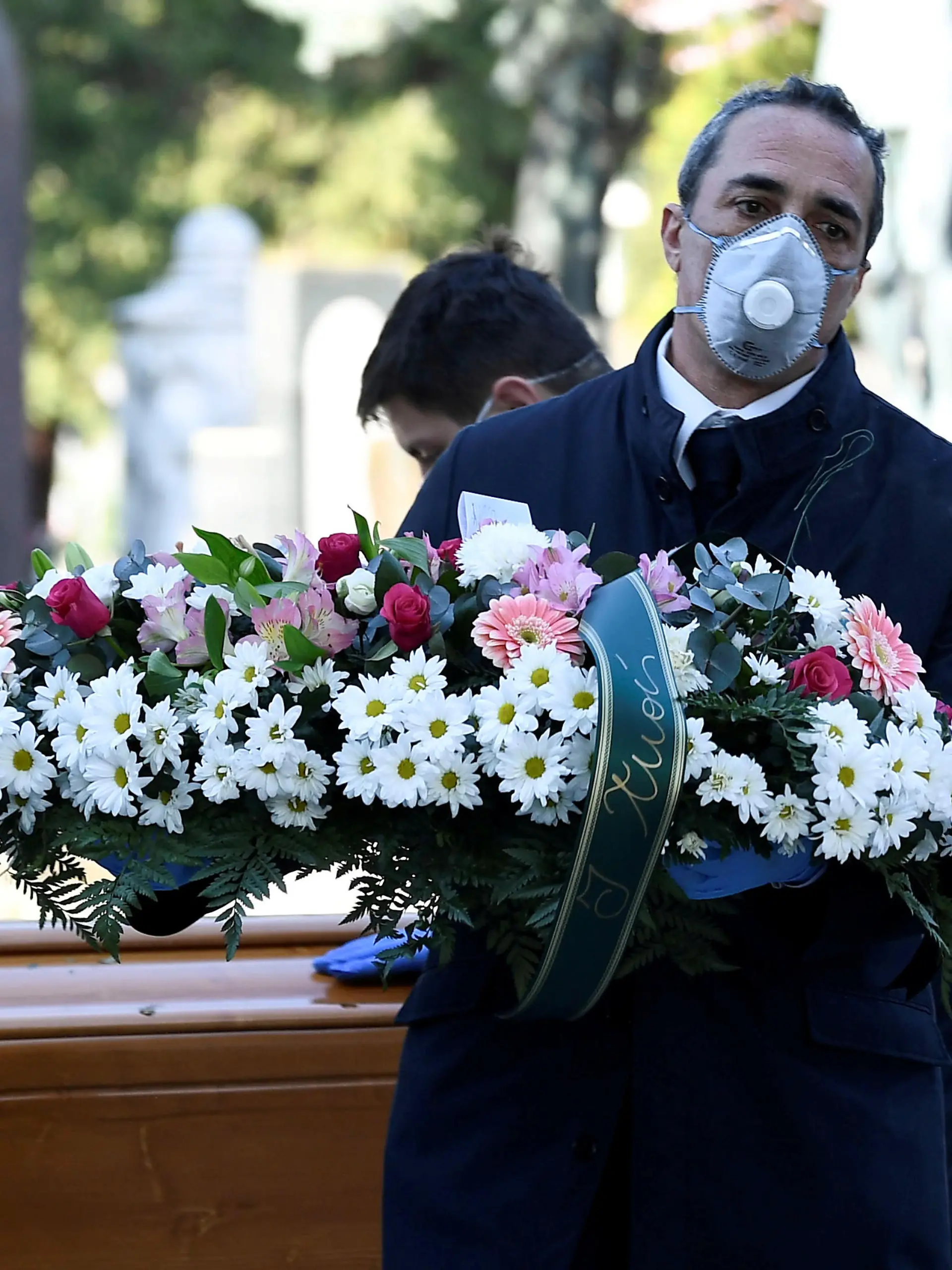 FILE PHOTO: Cemetery workers and funeral agency workers in protective masks transport a coffin of a person who died from coronavirus disease (COVID-19), into a cemetery in Bergamo, Italy March 16, 2020. REUTERS/Flavio Lo Scalzo/File Photo