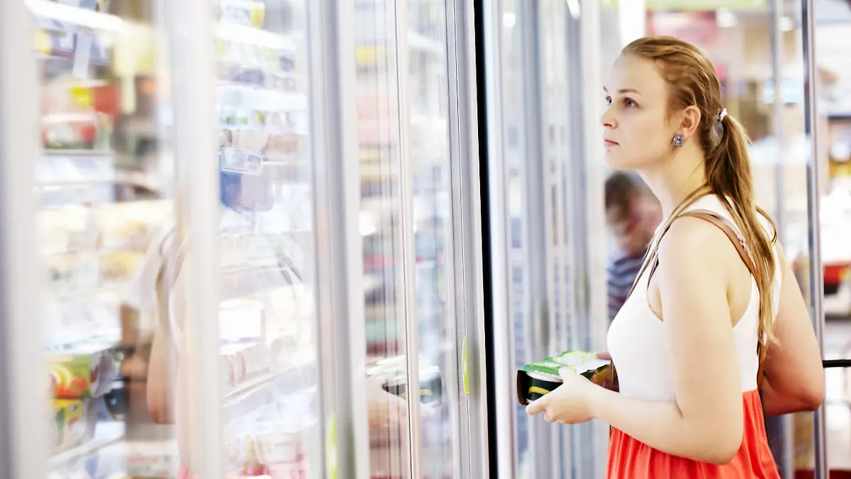 Young woman buying dairy or refrigerated groceries at the supermarket in the refrigerated section opening glass door of the fridge