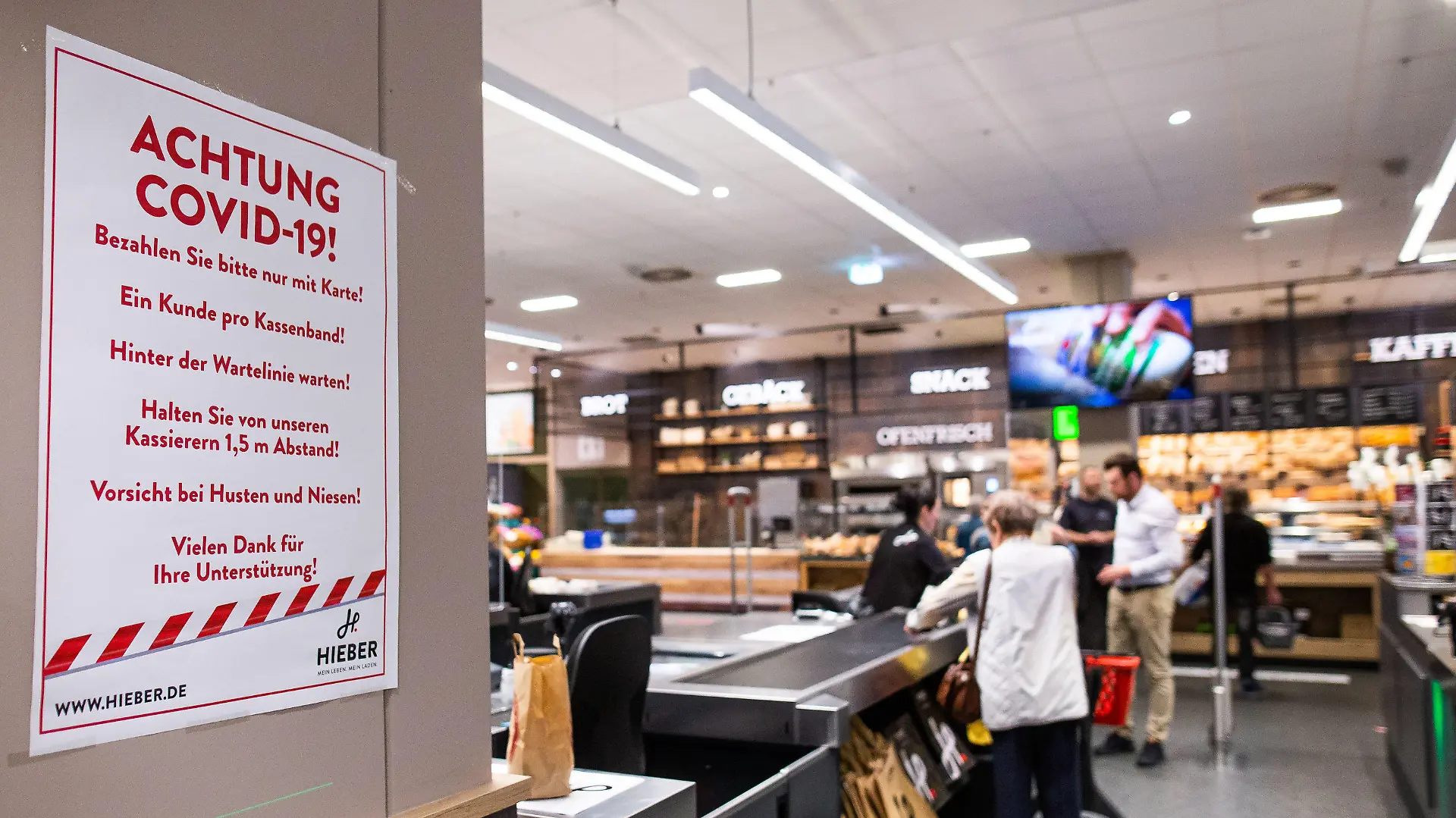 20.03.2020, Baden-Württemberg, Rheinfelden: Ein Hinweisschild mit der Überschrift "Achtung Covid-19" hängt im Kassenbereich eines Supermarktes. Der Einzelhandel ist durch die Coronavirus-Pandemie derzeit stark gefordert und trifft vielerorts Maßnahmen gegen die weitere Ausbreitung. Foto: Philipp von Ditfurth/dpa +++ dpa-Bildfunk +++