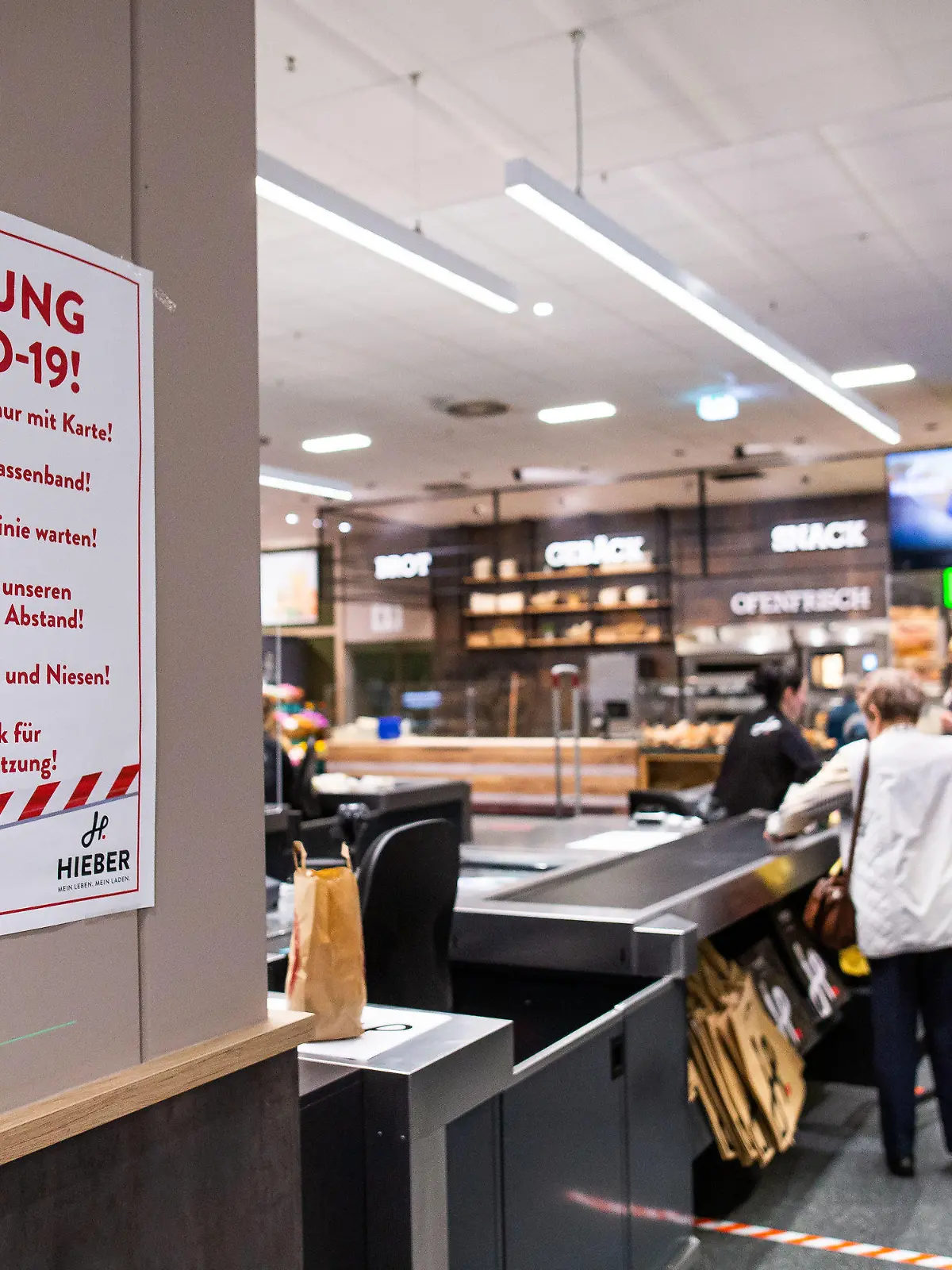 20.03.2020, Baden-Württemberg, Rheinfelden: Ein Hinweisschild mit der Überschrift "Achtung Covid-19" hängt im Kassenbereich eines Supermarktes. Der Einzelhandel ist durch die Coronavirus-Pandemie derzeit stark gefordert und trifft vielerorts Maßnahmen gegen die weitere Ausbreitung. Foto: Philipp von Ditfurth/dpa +++ dpa-Bildfunk +++