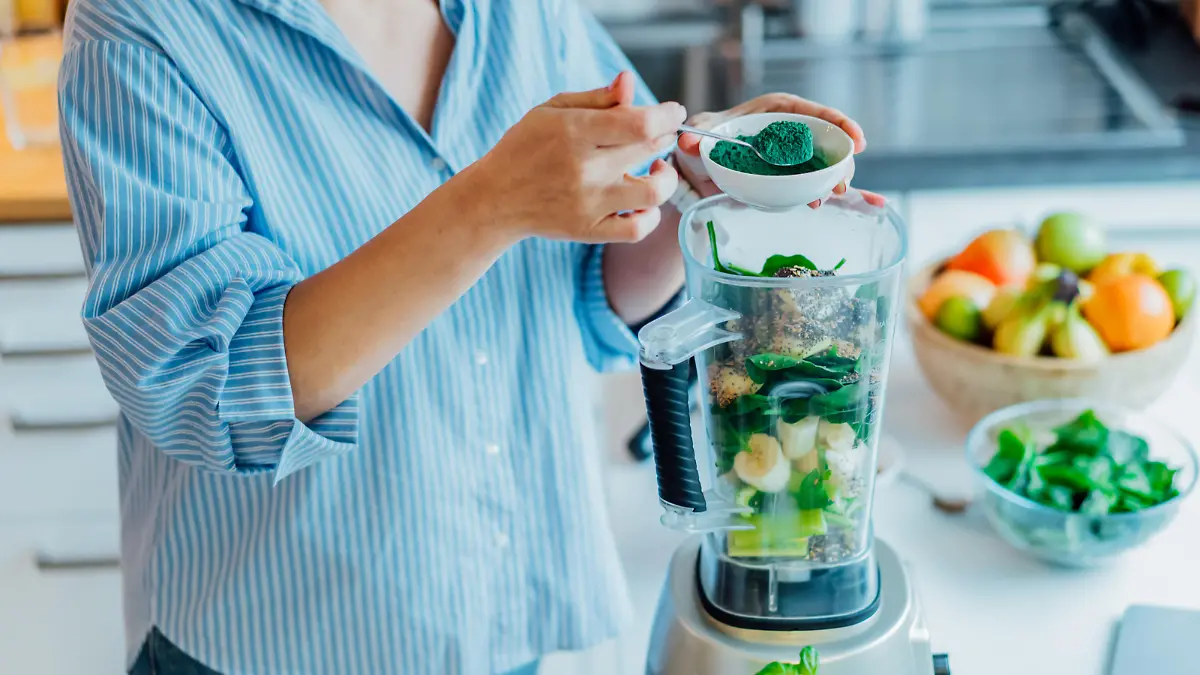 Woman adding spirulina green powder during making green smoothie on the kitchen. Superfood supplement. Healthy detox vegan diet. Healthy dieting eating, weight loss program. Selective focus