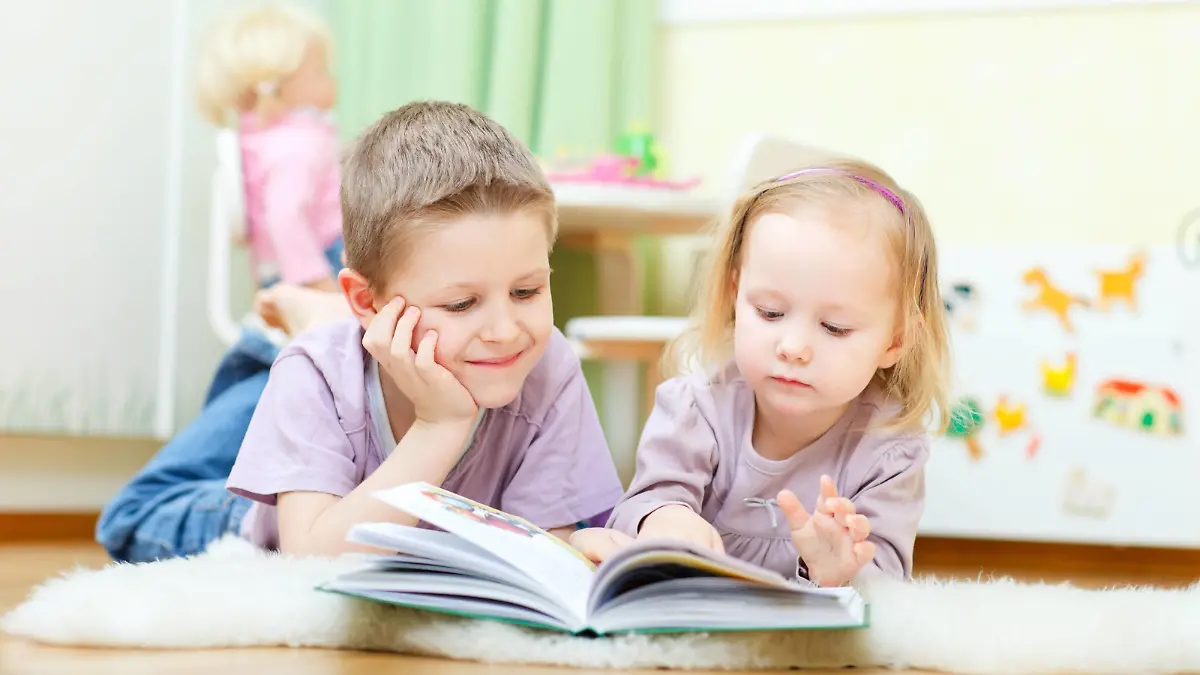 Bruder und Schwester liegen im Kinderzimmer auf dem Boden und lesen zusammen ein Buch | brother and sister lying on the floor in their nursery reading a book together