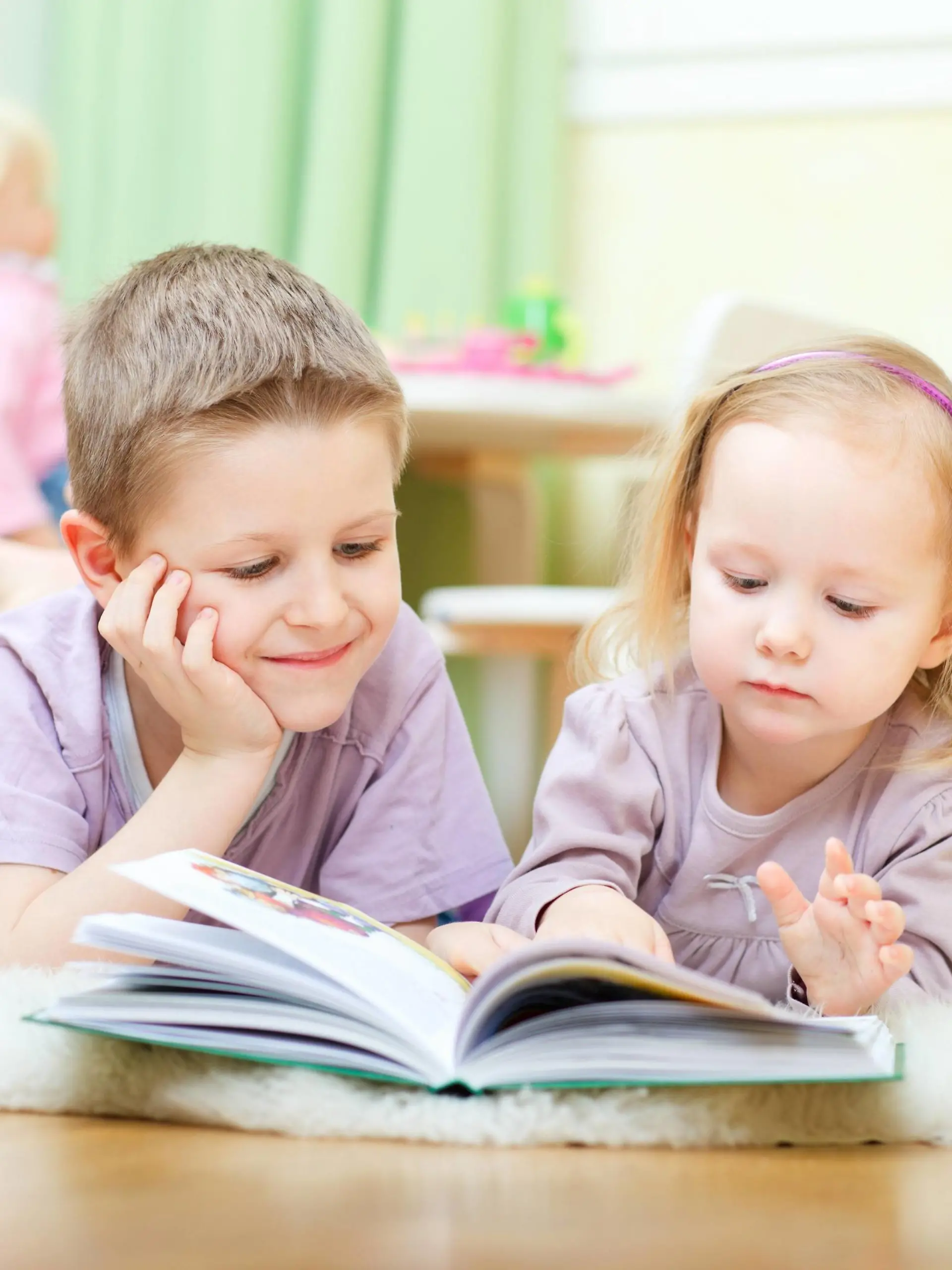 Bruder und Schwester liegen im Kinderzimmer auf dem Boden und lesen zusammen ein Buch | brother and sister lying on the floor in their nursery reading a book together