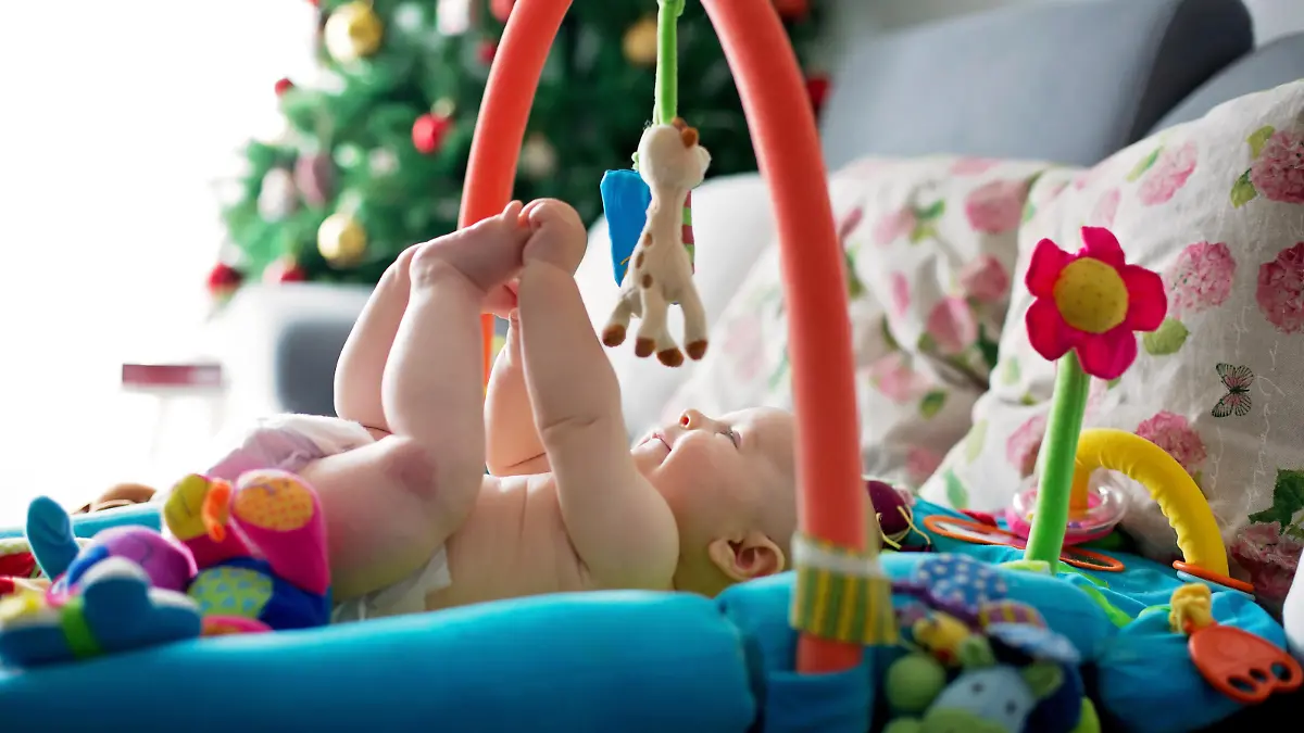 Das Baby liegt unter dem Babygym und erfreut sich an den bunten Anhängern.