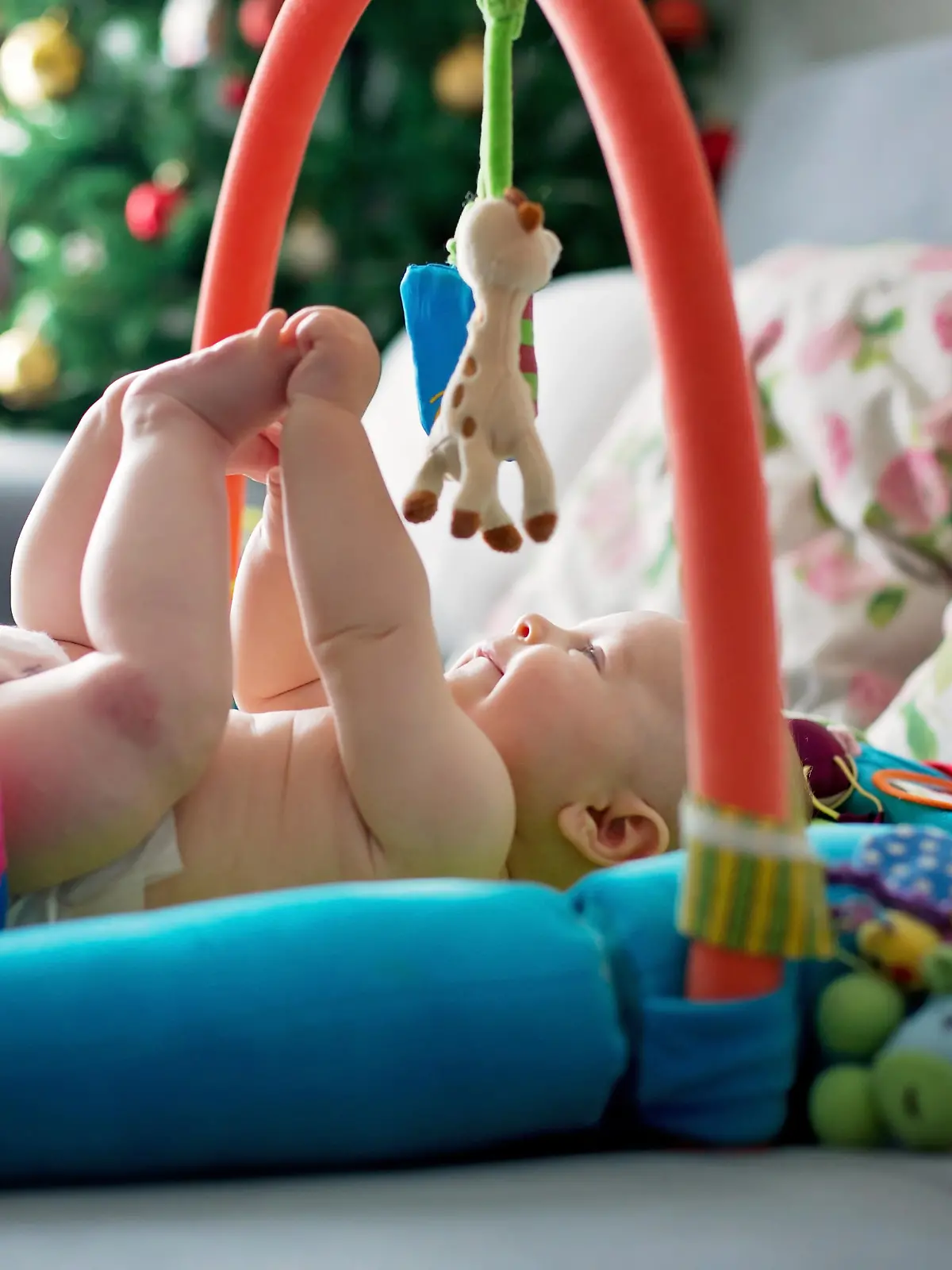 Das Baby liegt unter dem Babygym und erfreut sich an den bunten Anhängern.