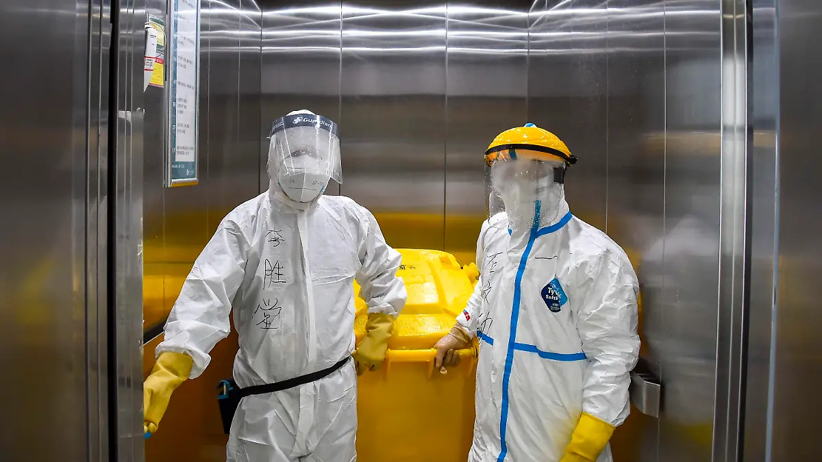 02.03.2020, China, Xiaogan: Li Shengtang (l) und Shi Wenqin, Mitarbeiter des Zentralkrankenhauses von Xiaogan, fahren mit Schutzkleidung in einem speziellen Fahrstuhl, um medizinischen Abfall zu entsorgen. In dem Krankenhaus werden vor allem die mit dem Coronavirus infizierten Patienten behandelt. Foto: Hu Huhu/XinHua/dpa +++ dpa-Bildfunk +++