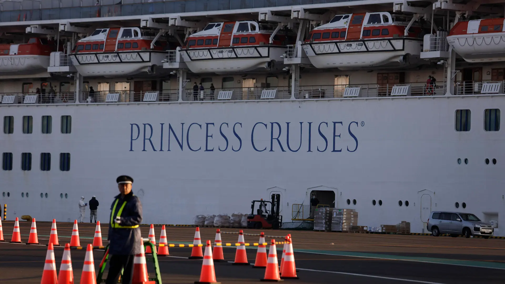 A security guard stands near the quarantined Diamond Princess cruise ship Thursday, Feb. 13, 2020, in Yokohama, near Tokyo. Life on board the luxury cruise ship, which has dozens of cases of a new virus, can include fear, excitement and soul-crushing boredom, according to interviews by The Associated Press with passengers and a stream of tweets and YouTube videos. (AP Photo/Jae C. Hong)
