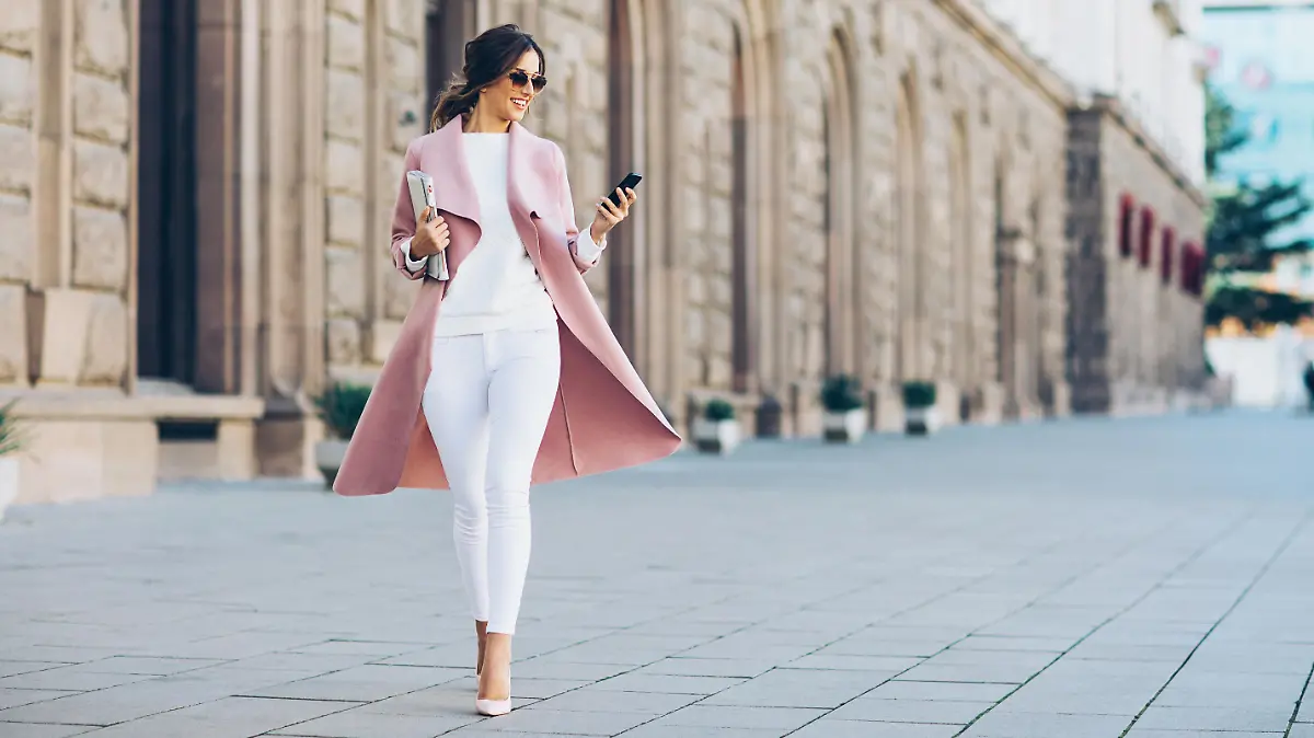Elegant young woman walking on the square and texting in urban environment.