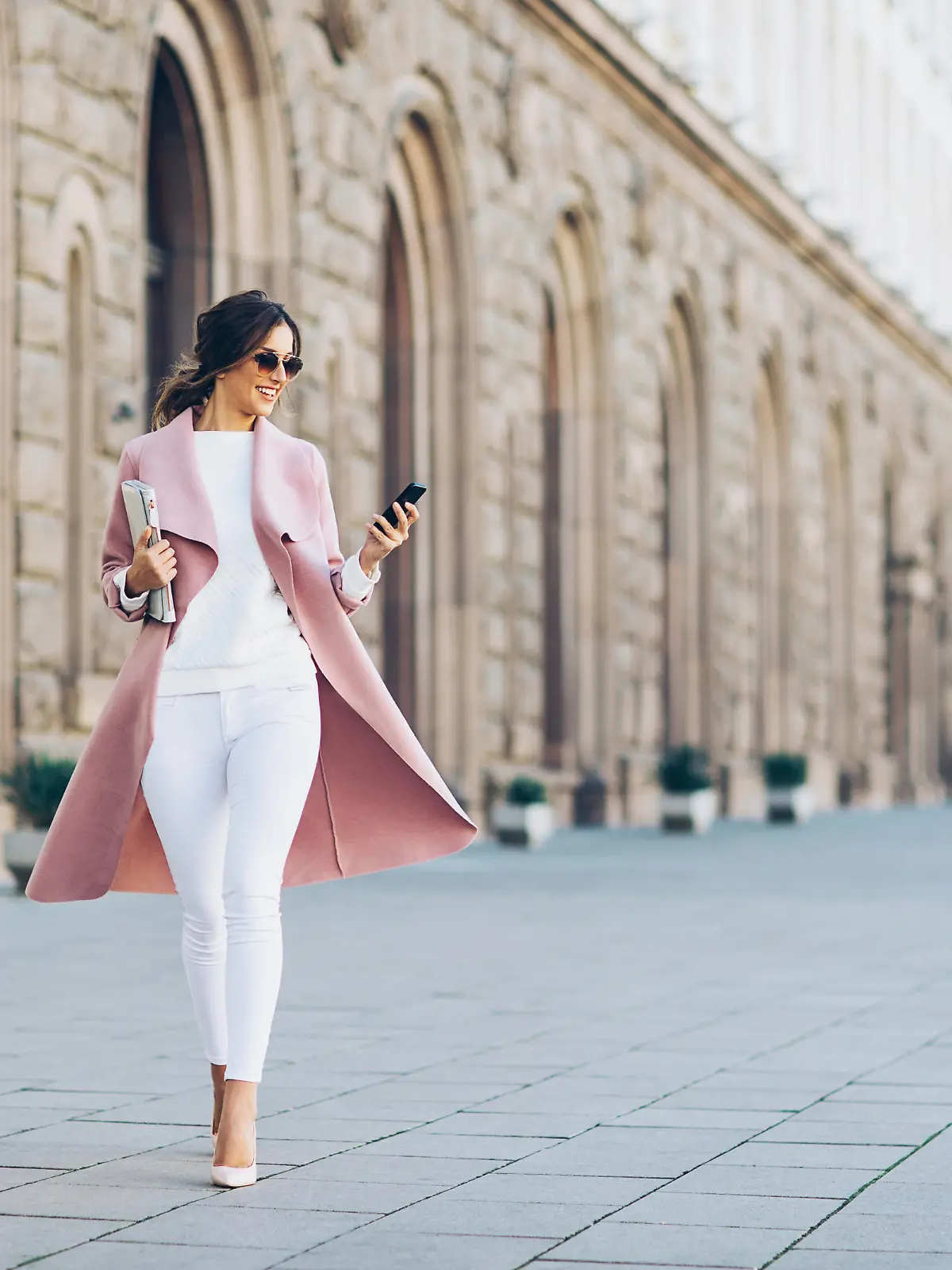 Elegant young woman walking on the square and texting in urban environment.