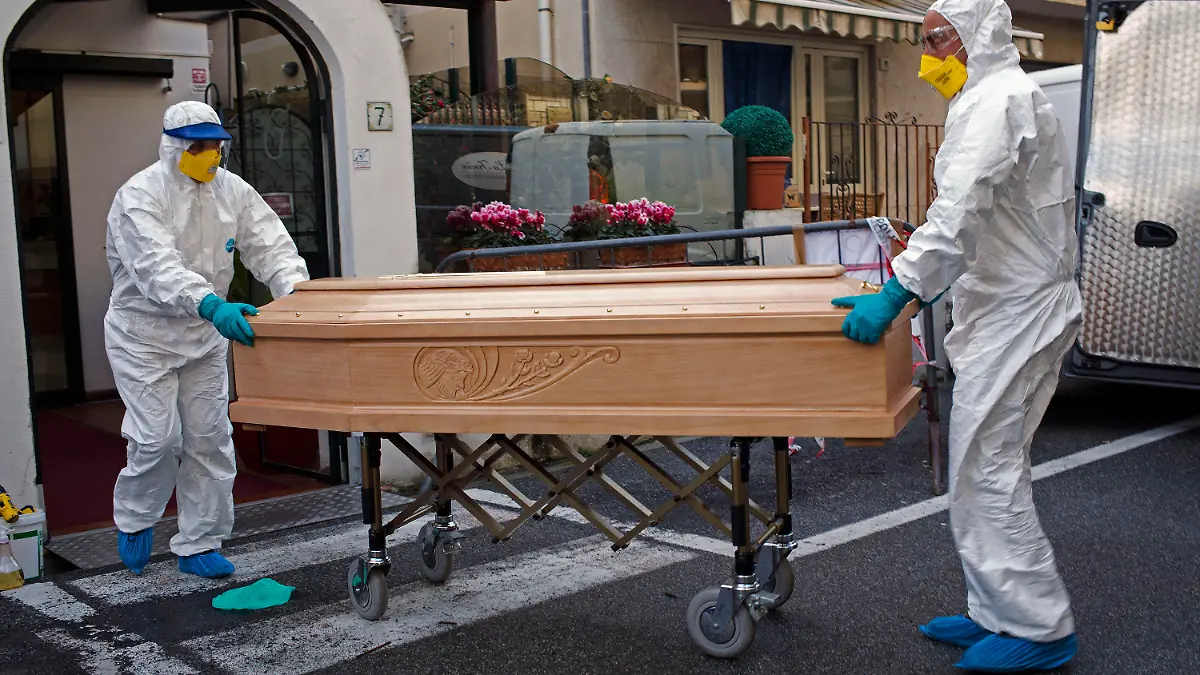 01.03.2020, Italien, Laigueglia: Medizinisches Personal in Schutzanzügen trägt einen Sarg mit dem Leichnam einer 87-jährigen Frau aus einem Hotel, nachdem sie in ihrem Zimmer verstorben ist. Die Frau, die zu einer Gruppe älterer Touristen aus der Region Lombardei gehörte, wurde positiv auf das Coronavirus getestet. Das Hotel wurde unter Quarantäne gestellt. Foto: AP/dpa +++ dpa-Bildfunk +++