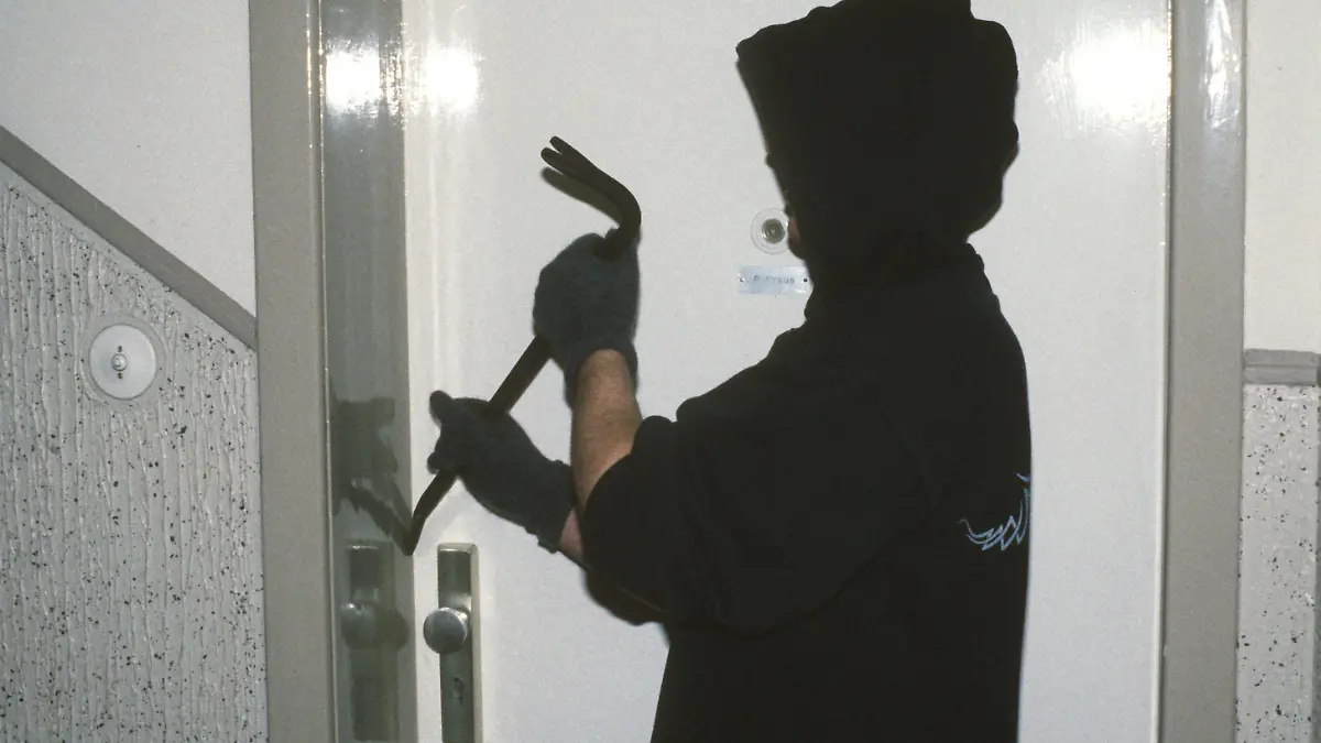 Ein vermummter Einbrecher mit Handschuhen macht sich mit einem Brecheisen an einer Wohnungstür in einem Mehrparteien-Mietshaus zu schaffen, aufgenommen im Januar 1994 (gestellte Einbruch-Szene).