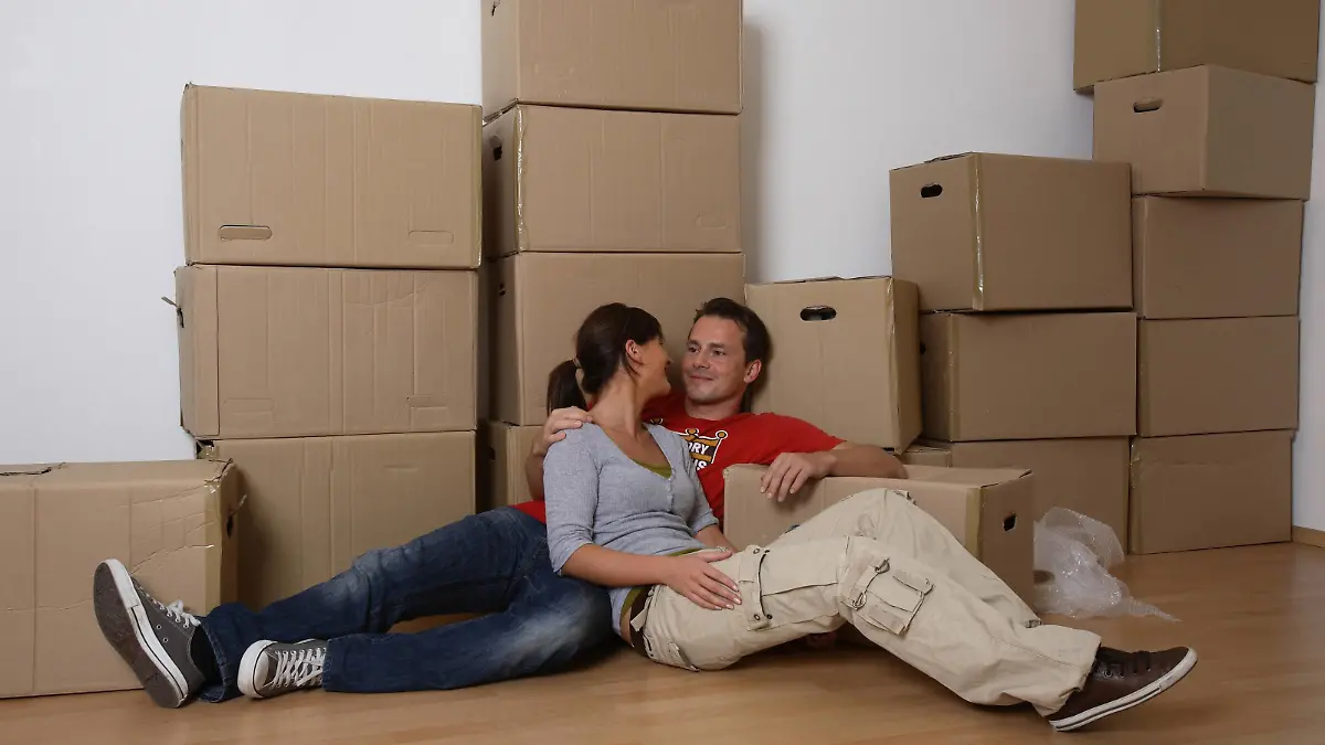 junges Paar beim Umzug sitzt am Boden, macht Pause und schaut sich verliebt an | young couple moving house and taking a break