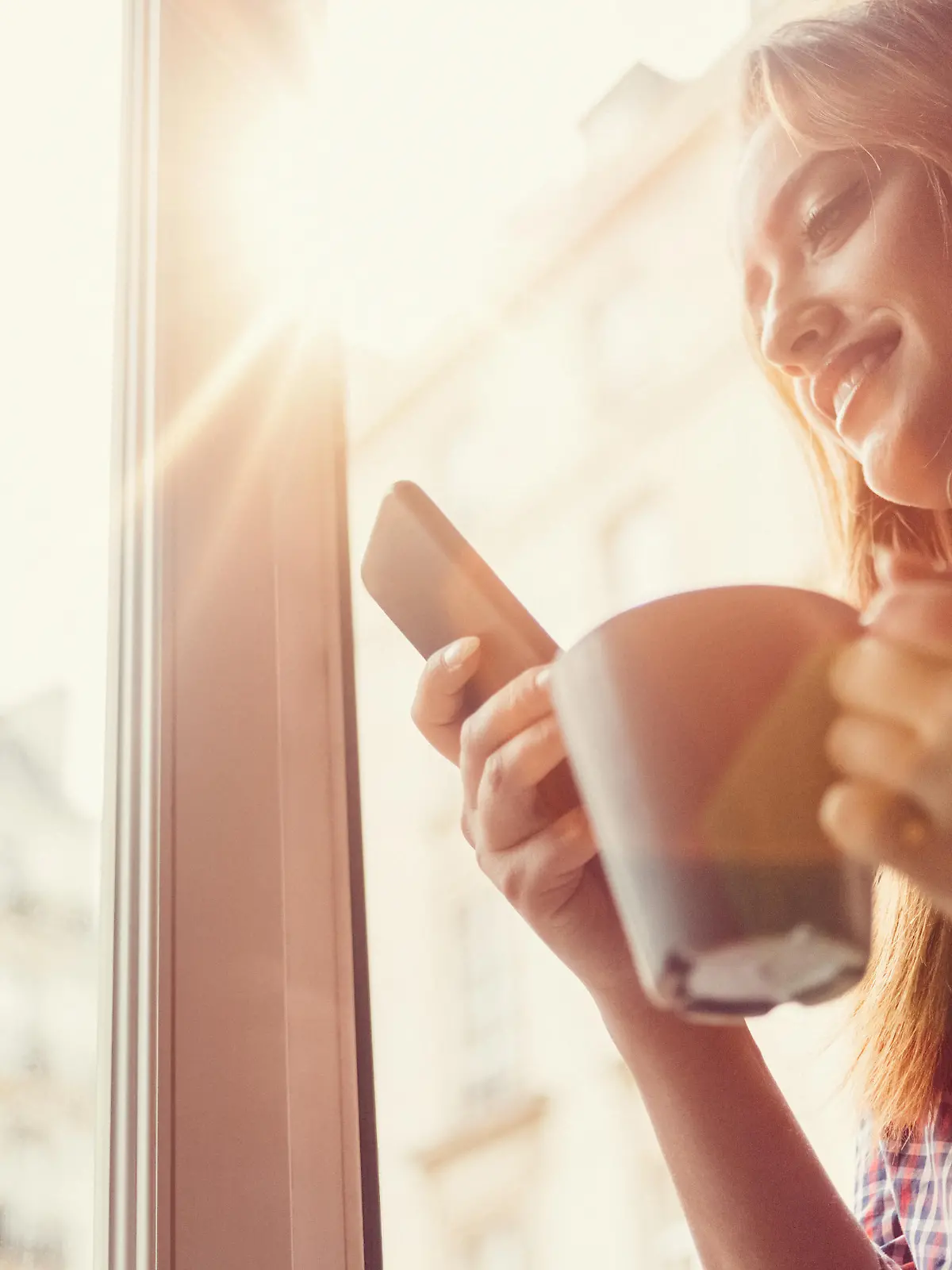 Smiling woman using smartphone and drinking coffee in the morning