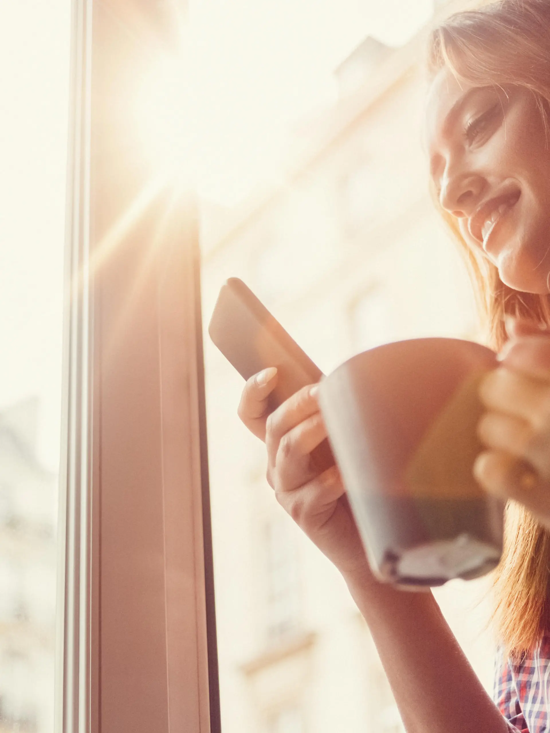 Smiling woman using smartphone and drinking coffee in the morning