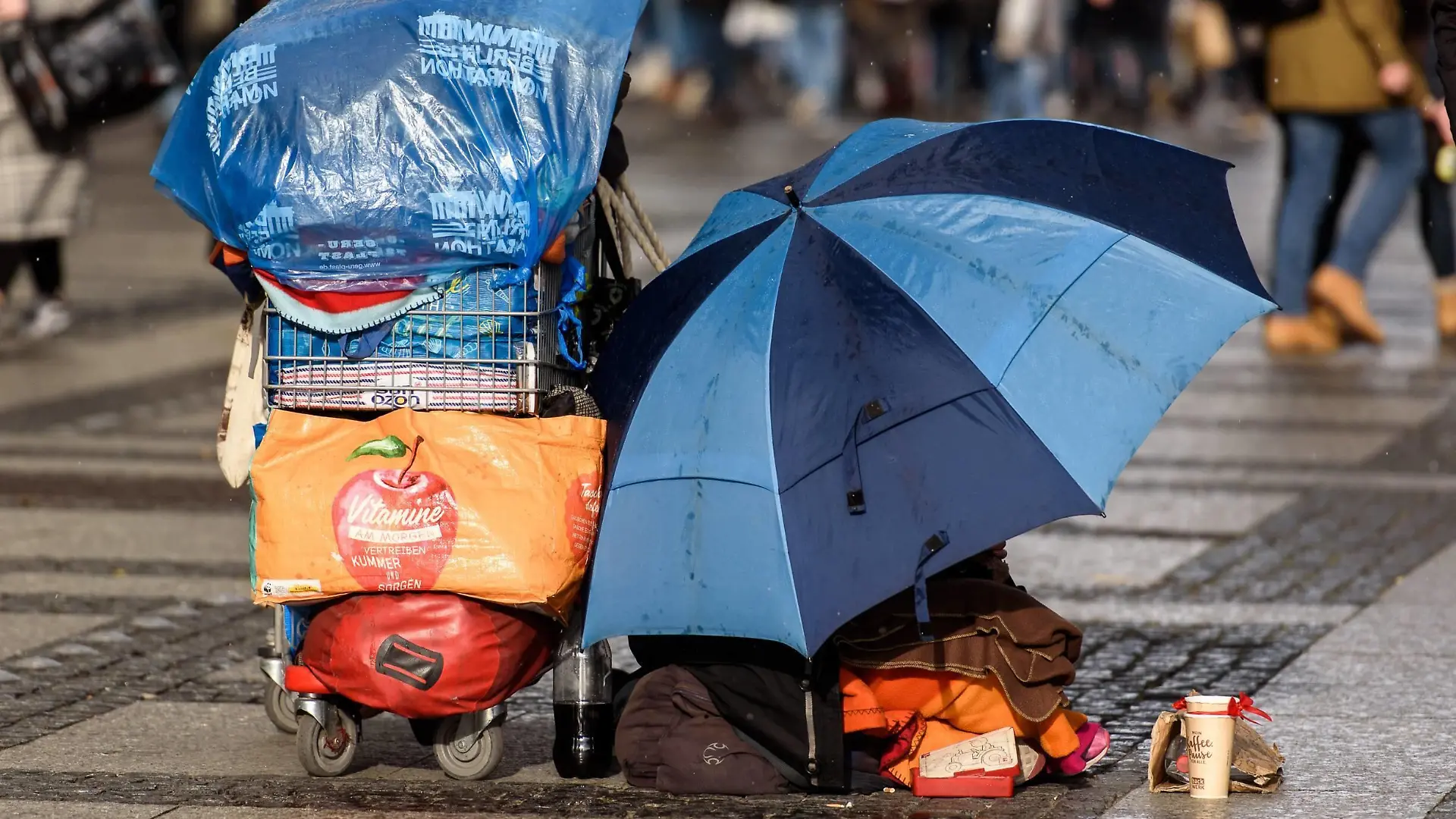 Feature Bild Obdachlosigkeit Deutschland, Berlin - 09/03/2019: Im Bild ist ein Obdachloser Mensch mit Schirm und Einkaufswagen sitzend auf der Straße zu sehen. Berlin Berlin Deutschland *** Feature Picture Homelessness Germany Berlin 09 03 2019 The picture shows a homeless person sitting on the street with an umbrella and a shopping trolley Berlin Berlin Berlin Germany