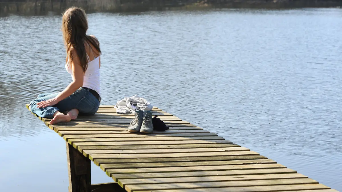 Eine junge Frau sitzt am 09.03.2014 bei frühlingshaftem Wetter auf einem Steg am Fährhofsee in Sottrum (Niedersachsen). Foto: Ingo Wagner/dpa +++(c) dpa - Bildfunk+++